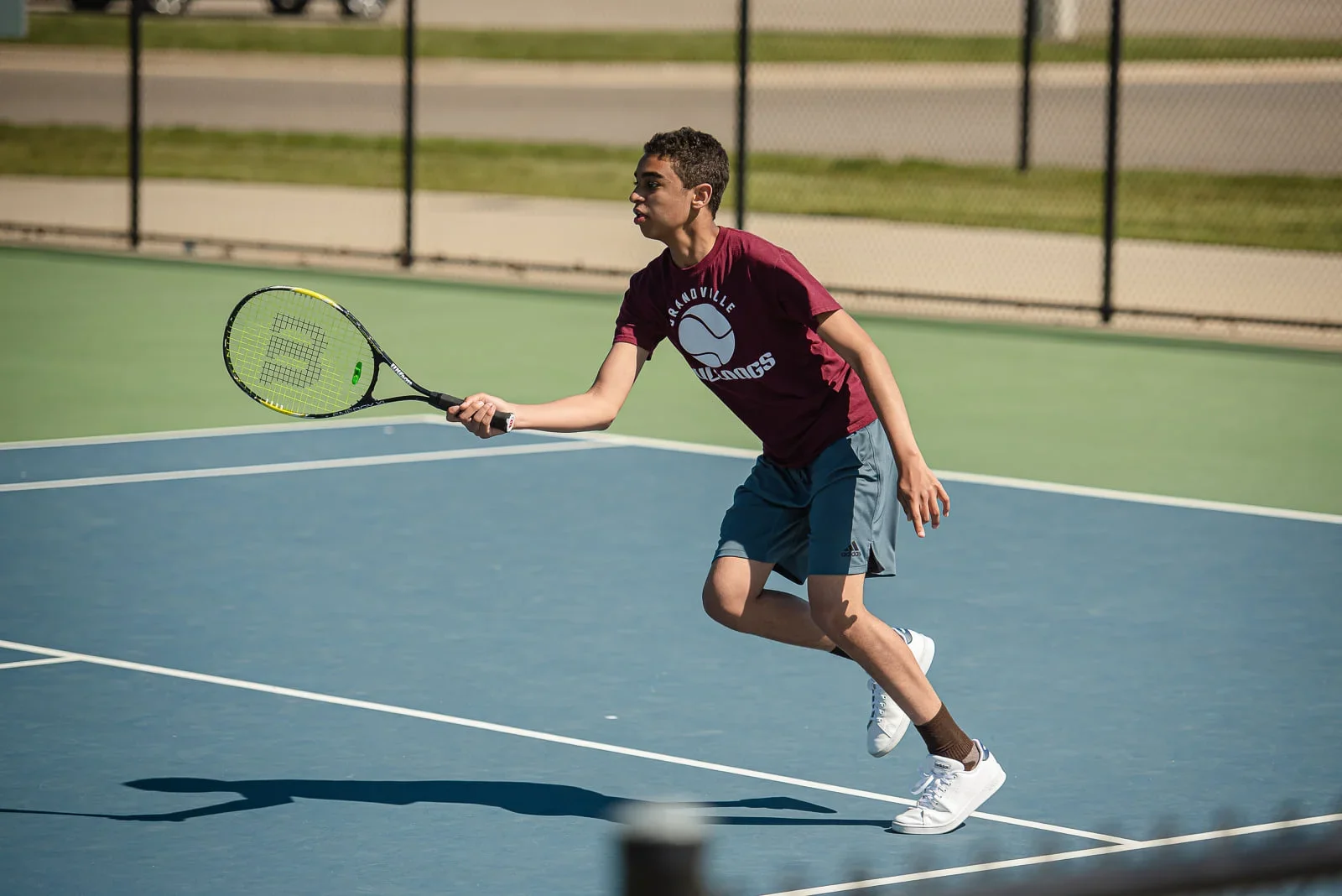 A young man playing tennis on an outdoor court, ready to hit a shot with a tennis racket.