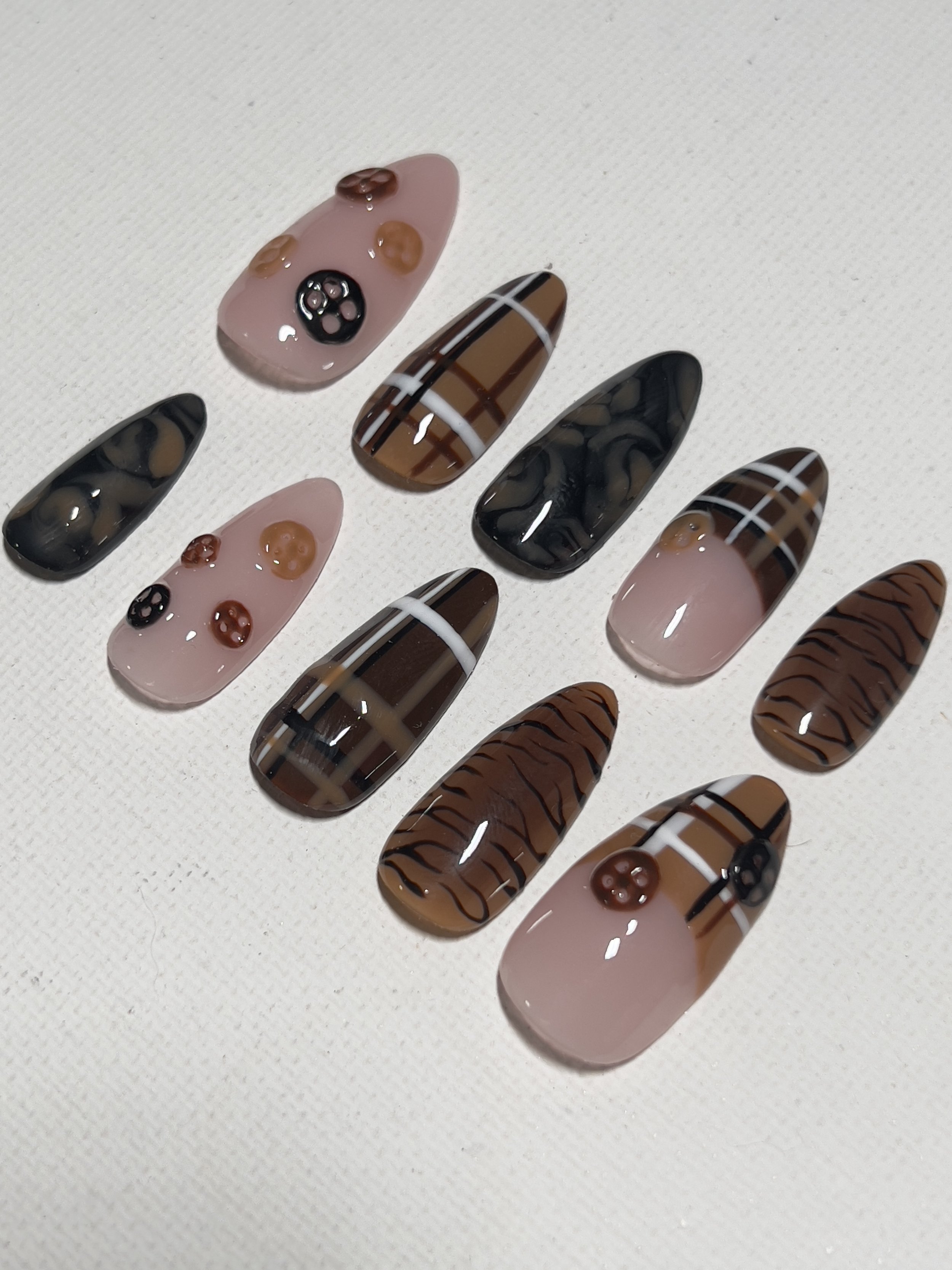 Set of decorative press-on nails with various patterns, including solid pink, black with buttons, plaid, and tiger stripe designs.
