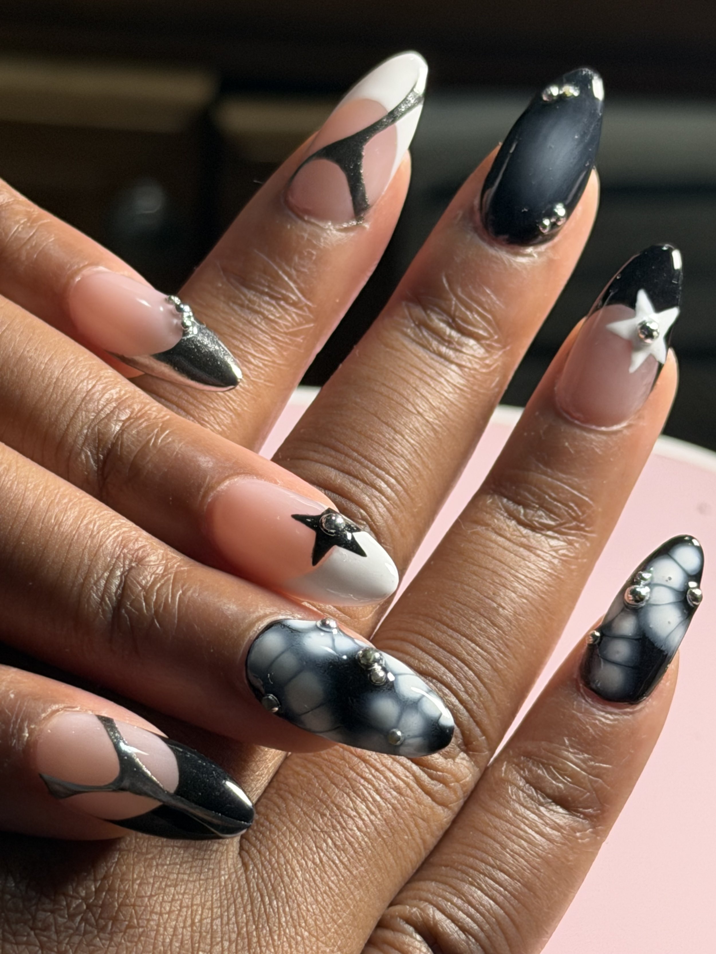 Close-up of a hand displaying intricately designed black and white nail art with metallic accents and 3D embellishments.