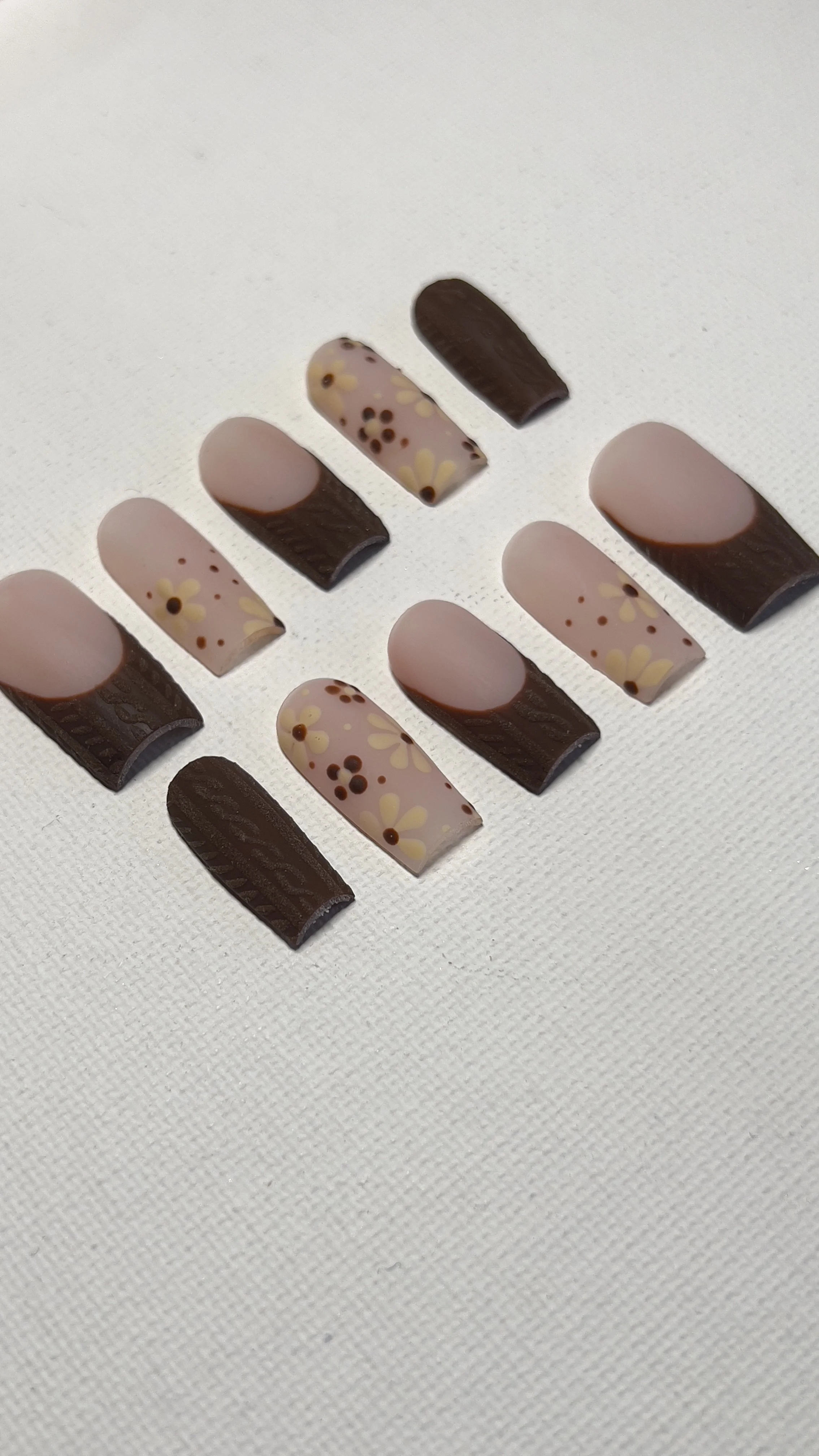 Assorted decorated artificial nails with floral designs and chocolate-like tips arranged on a white surface.