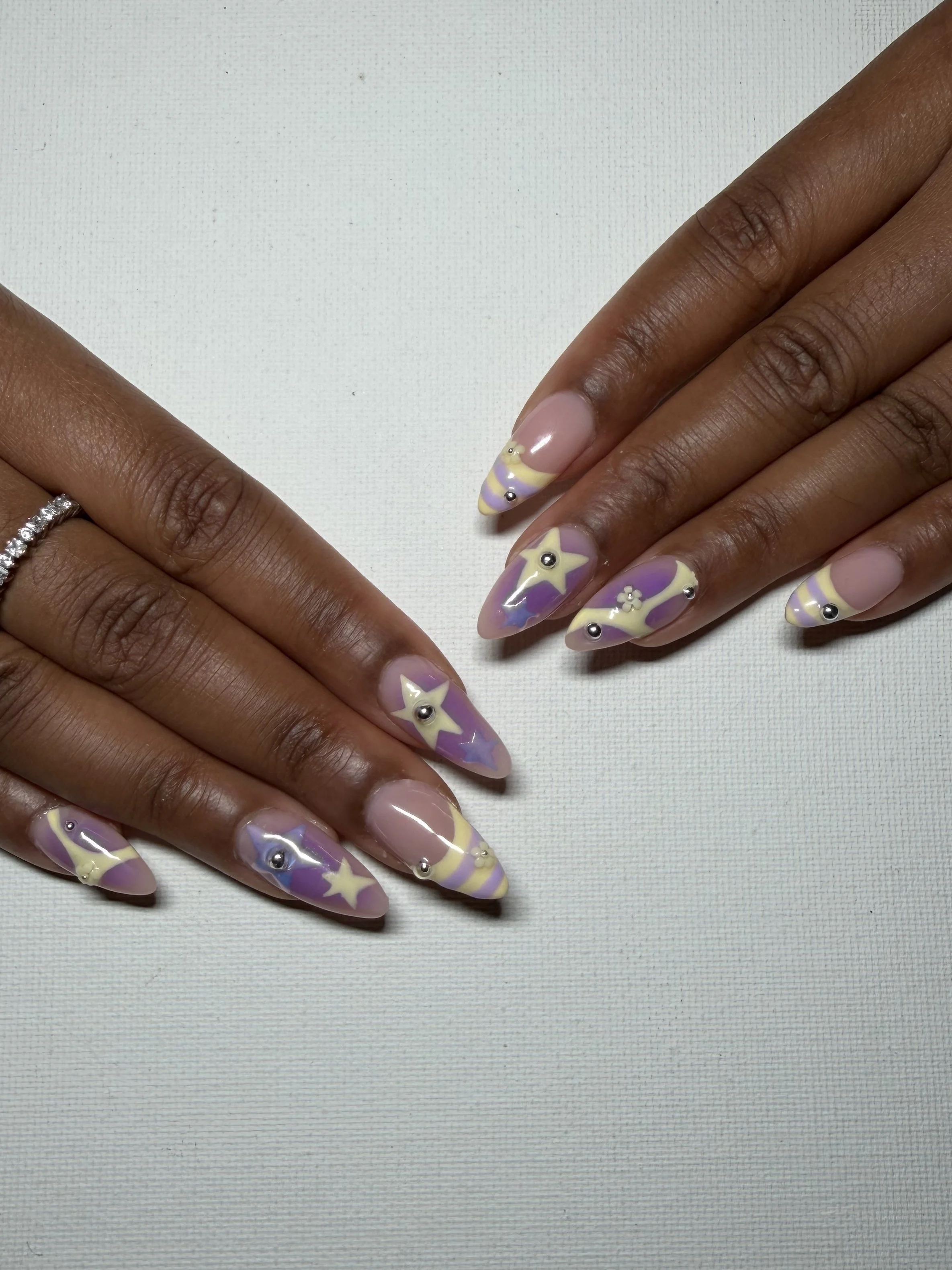 Close-up of hands with decorated, star and moon themed nail art on long, almond-shaped nails, set against a white textured background.