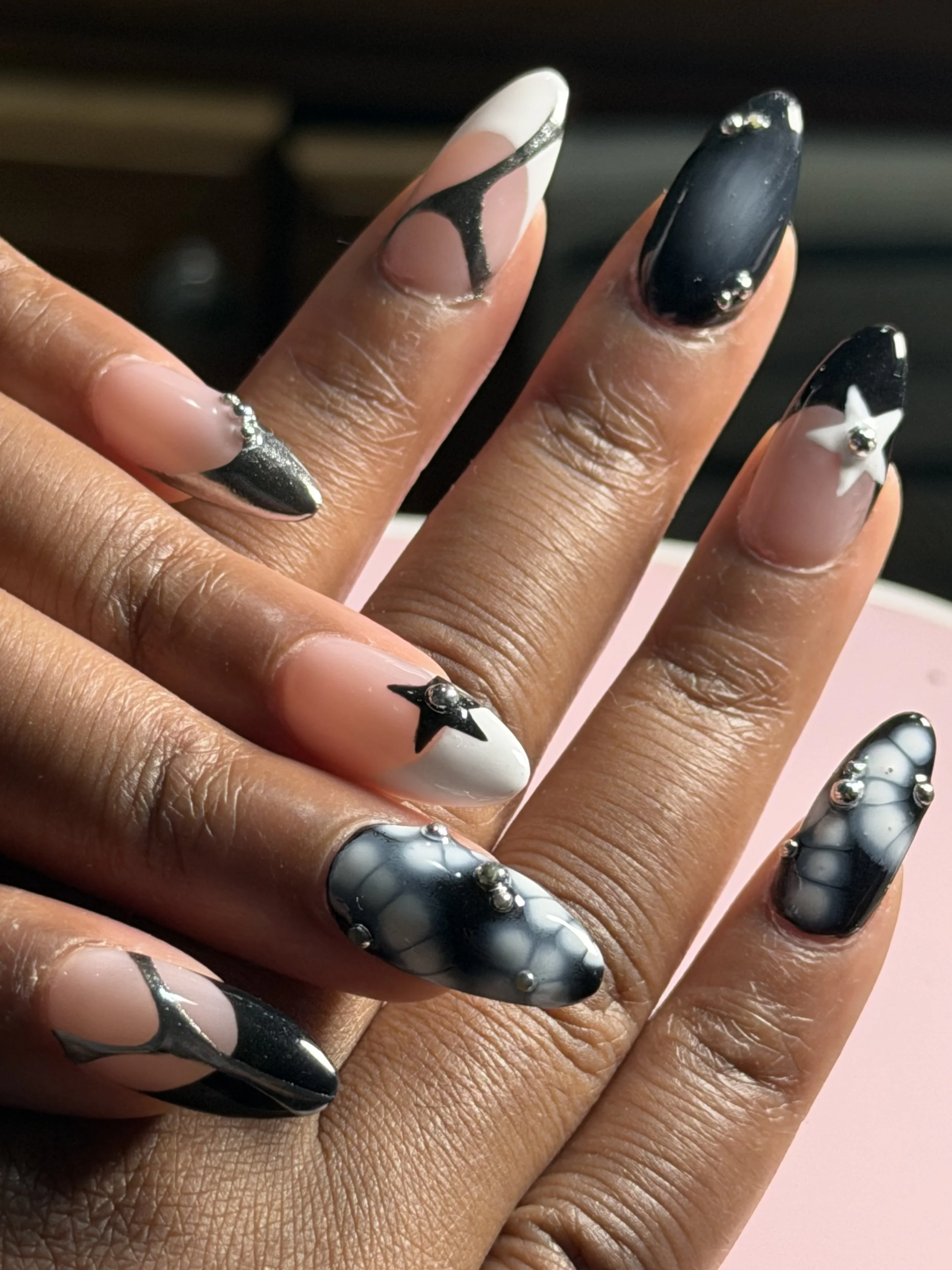 Close-up of a hand with decorated nails featuring silver, black, white, and star designs with 3D embellishments.