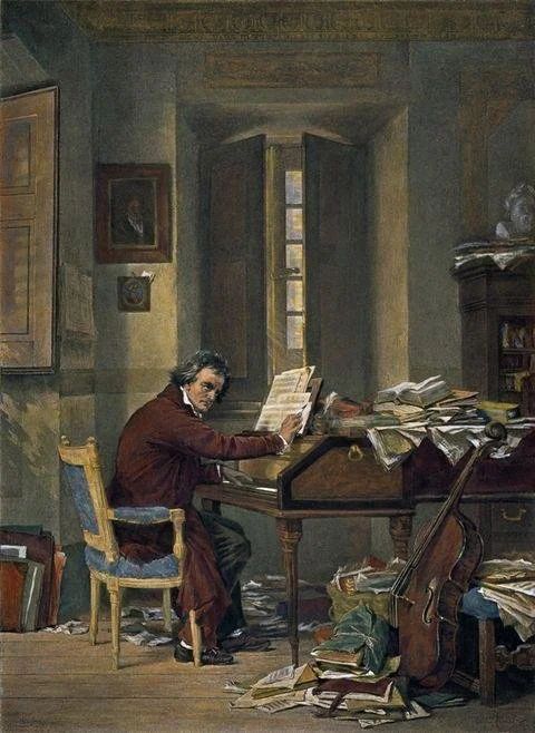 Un hombre sentado en una habitación llena de libros y papeles, leyendo un libro, con una ventana al fondo y una silla al lado.