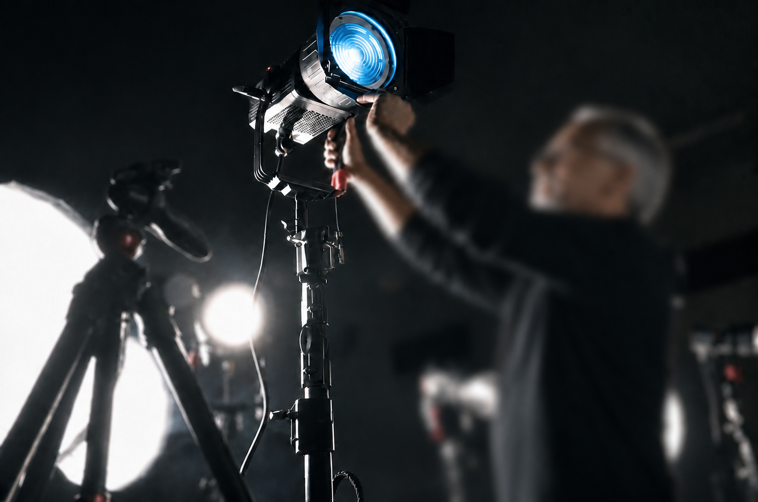 Person holding a professional studio light pointing upwards in a dark studio, with a camera on a tripod in the background.