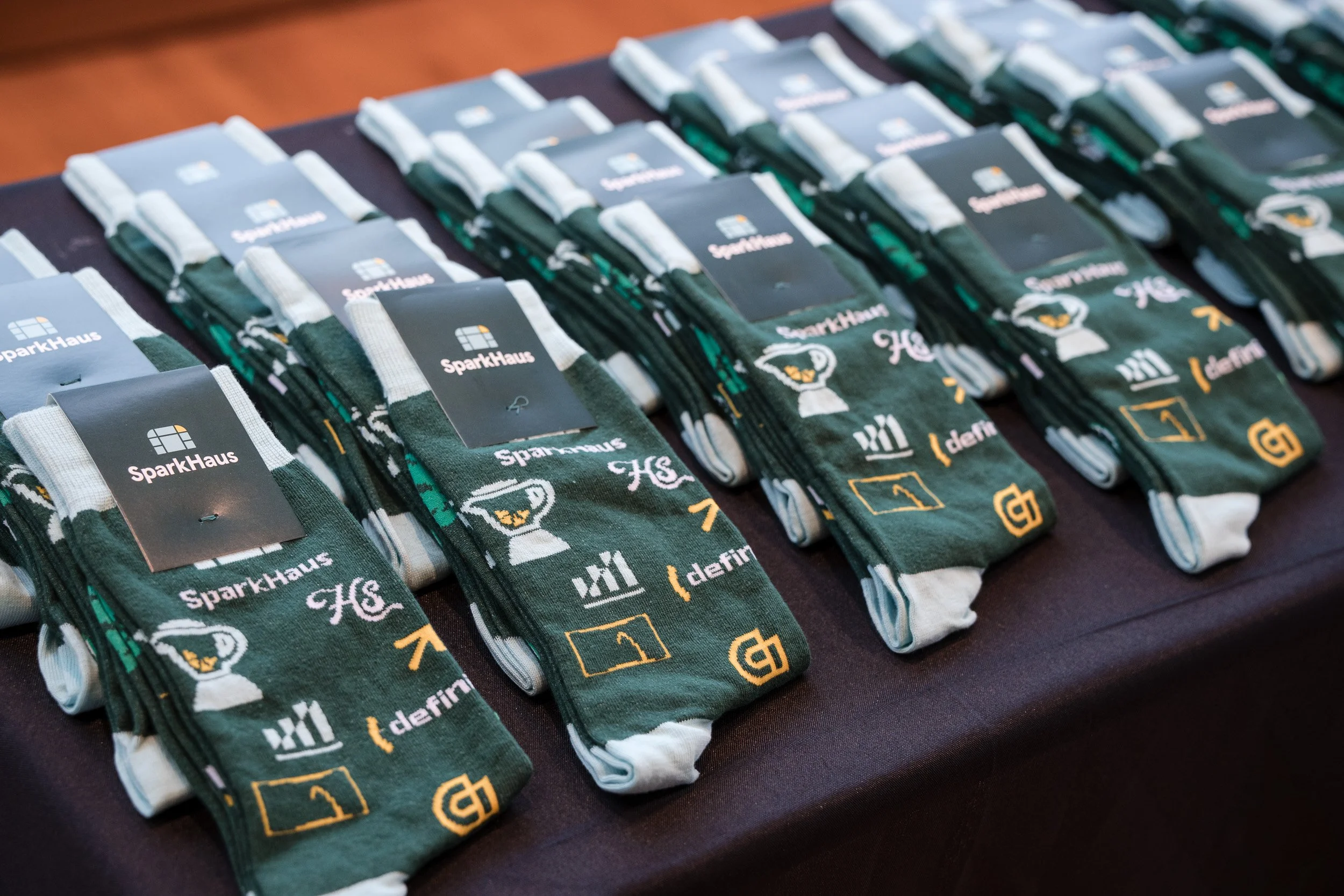 Multiple pairs of socks with the SparkHaus logo and various icons, arranged in rows on a dark surface.