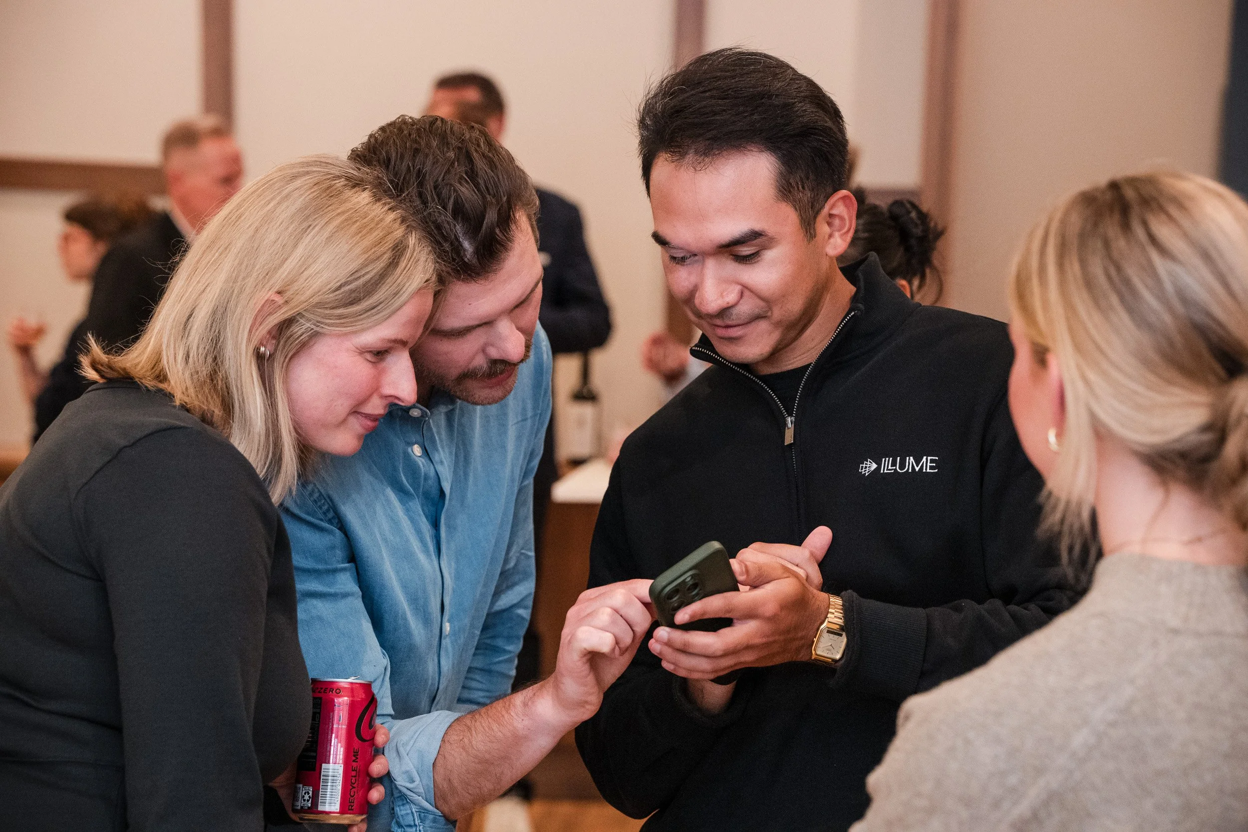 Group of five people gathered closely around looking at a smartphone, in a professional or social setting.