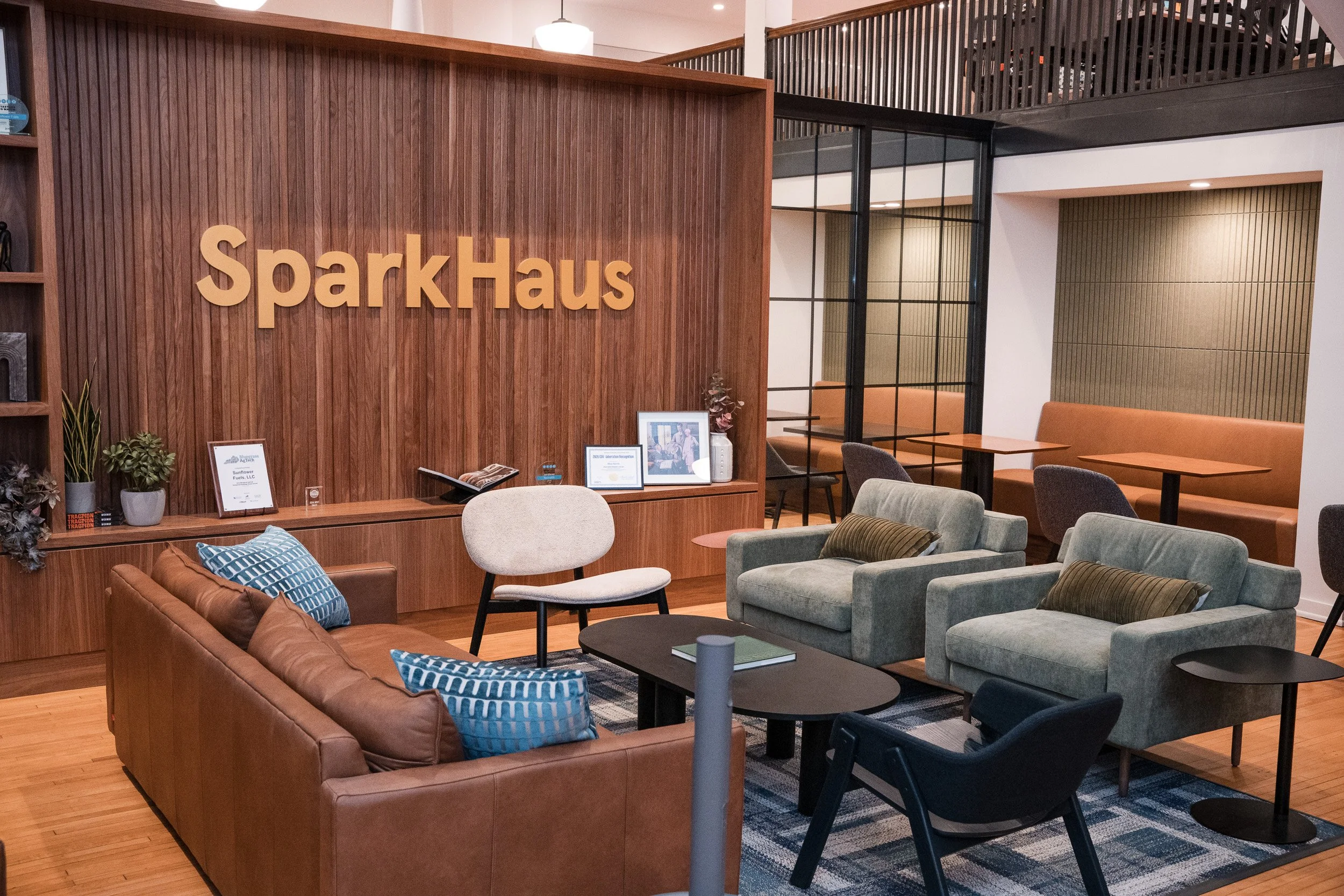 Interior of a modern coworking space with seating area, wooden accents, plants, and a sign reading 'SparkHaus' on a wooden wall.