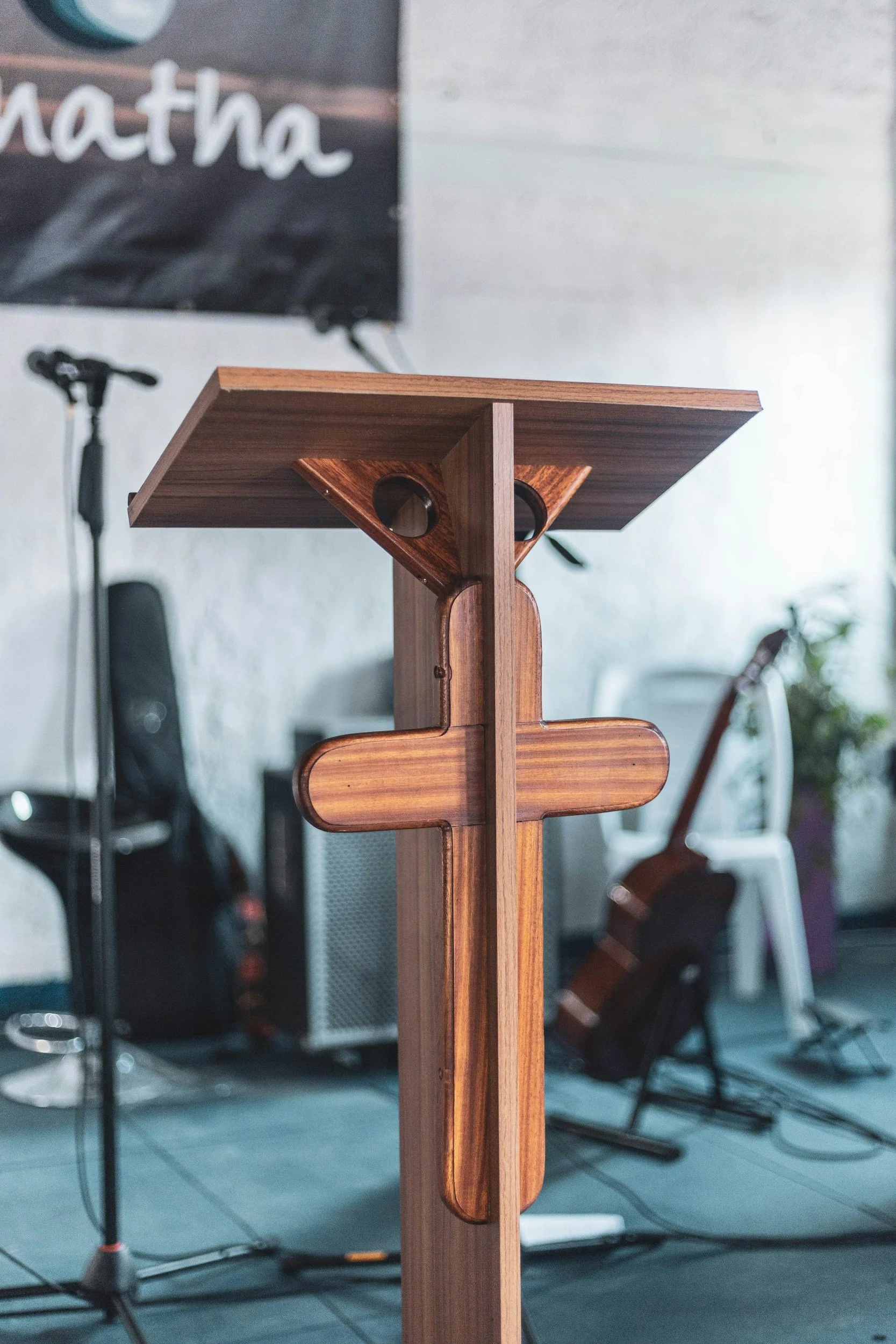 Close-up of a wooden lectern or podium with a curved cutout on the front, in a room with a microphone, bicycle, and various electronic equipment in the background.