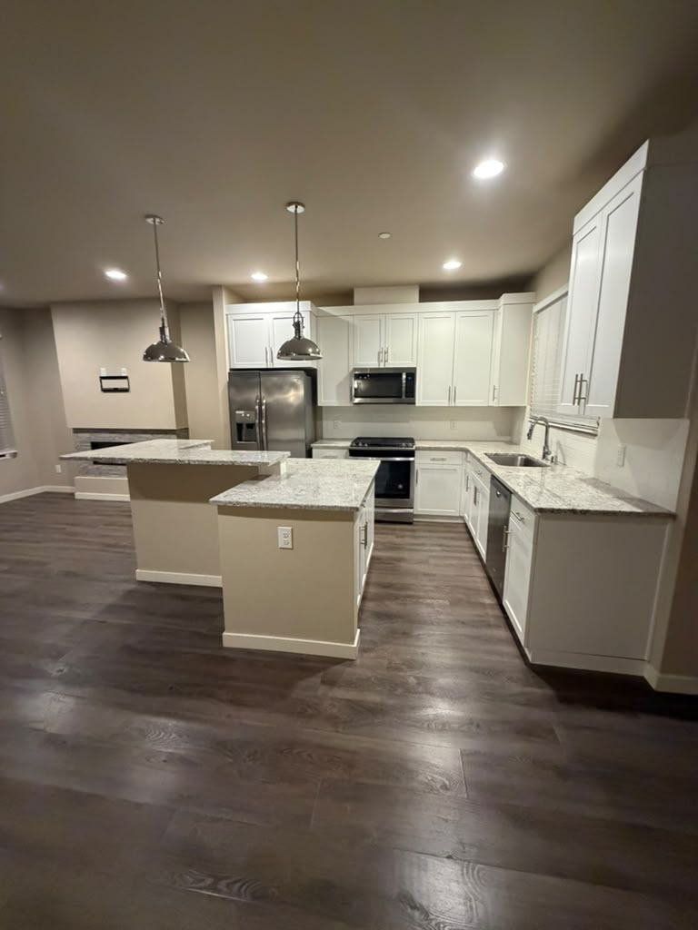 Modern kitchen with white cabinets, stainless steel appliances, granite countertops, and dark wood flooring.