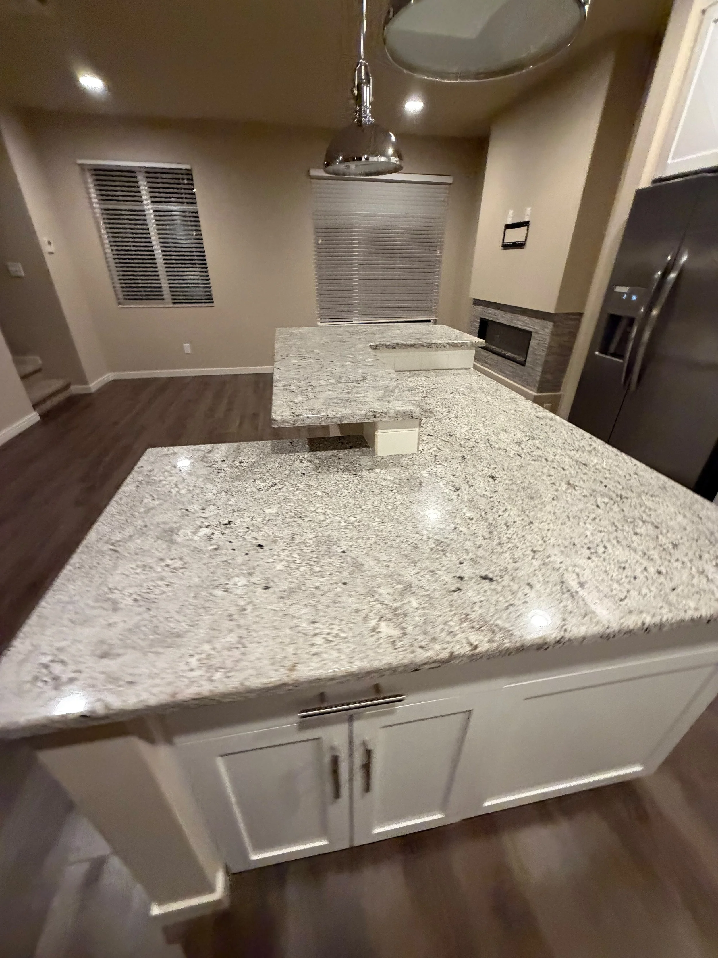 Kitchen countertop with granite surface, white cabinets below, and a stainless steel refrigerator to the right.