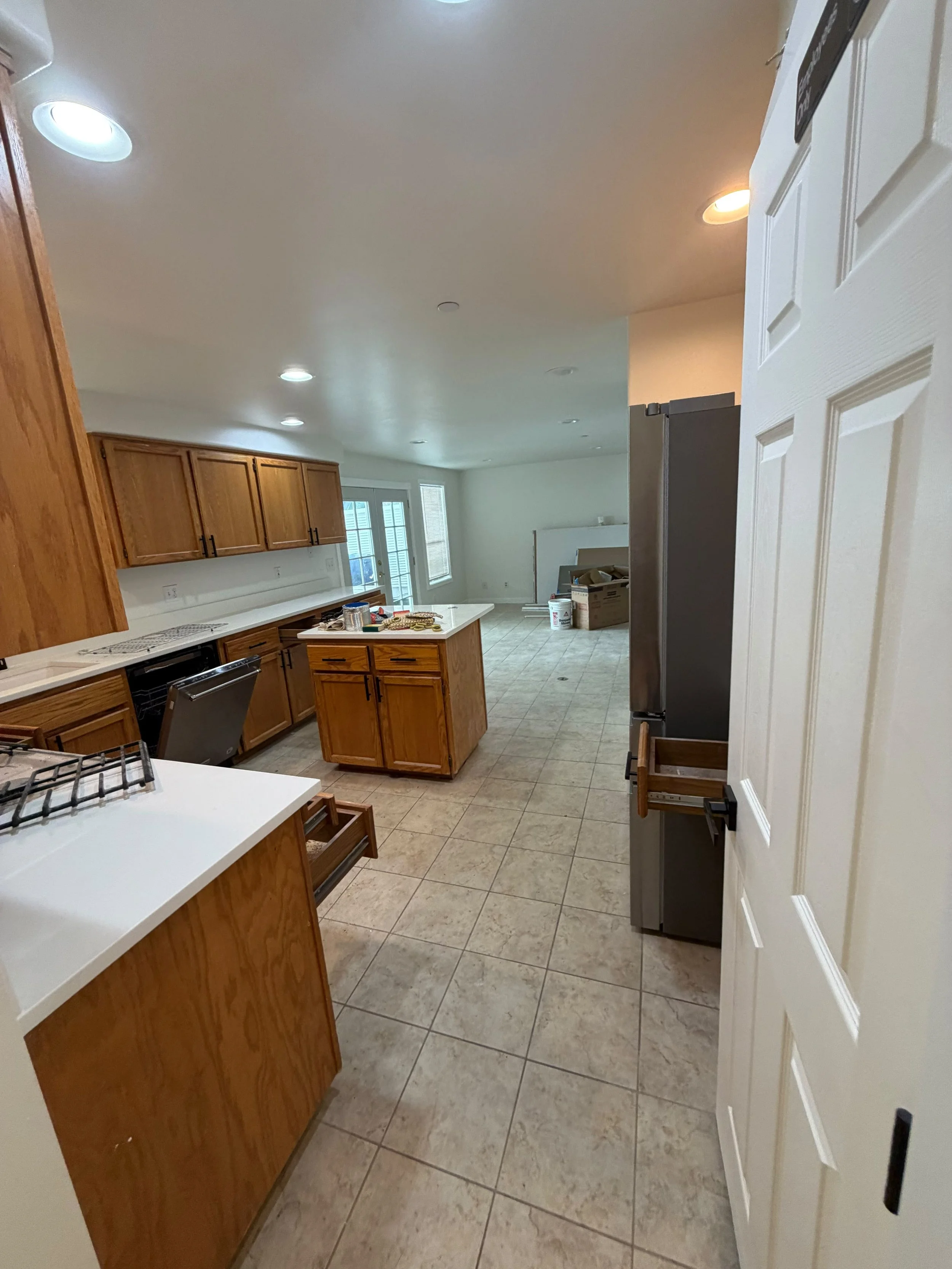 A kitchen under renovation with wooden cabinets, a white countertop, and a tiled floor, and some tools and materials on the counter.