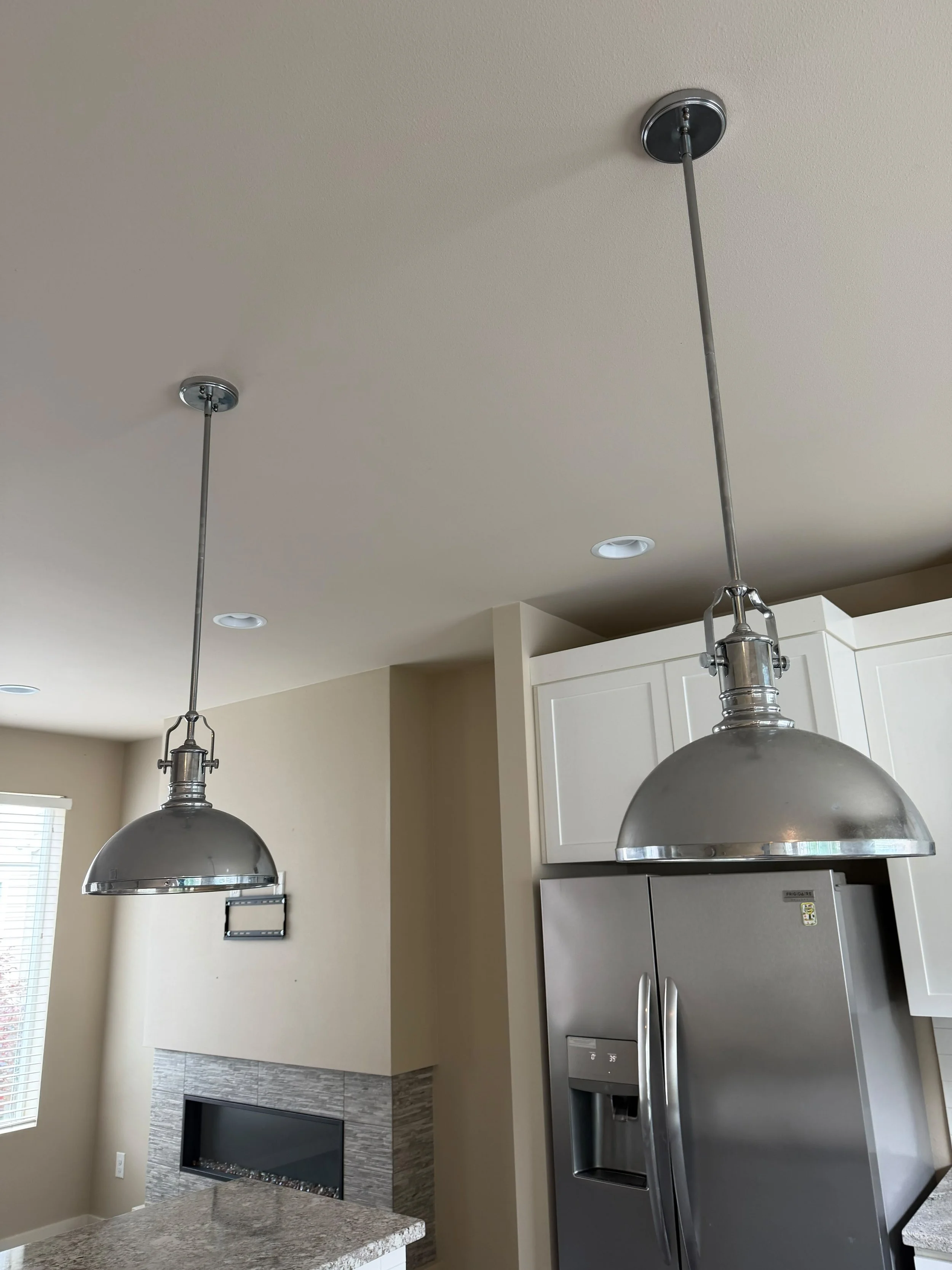 Kitchen with two hanging pendant lights, white cabinets, a stainless steel refrigerator with water and ice dispenser, and a modern fireplace in the living room area.