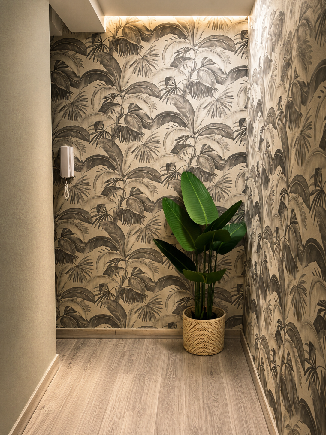Interior con pared de papel tapiz con estampado de hojas en tonos beige y gris, planta verde de gran tamaño en maceta de cestería
