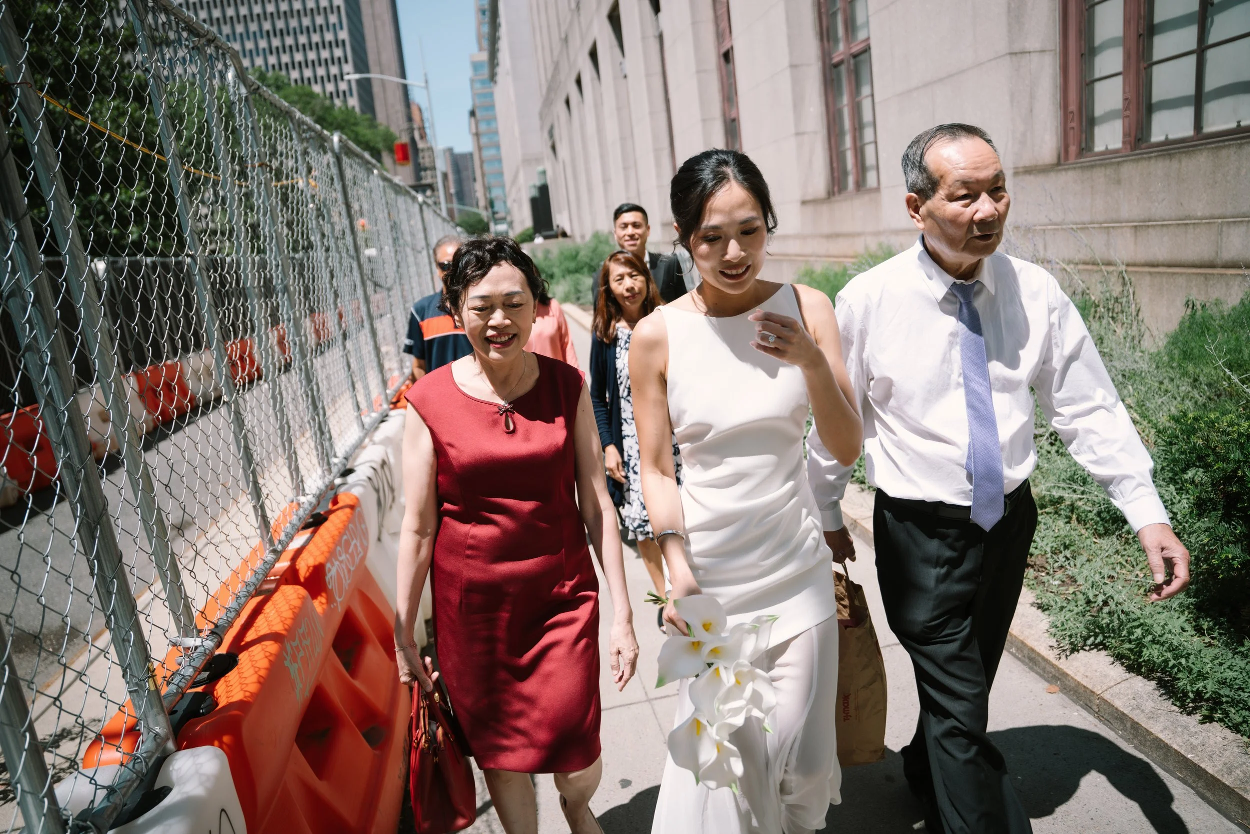 Group of people walking along a city sidewalk next to a construction barrier, with modern buildings in the background.