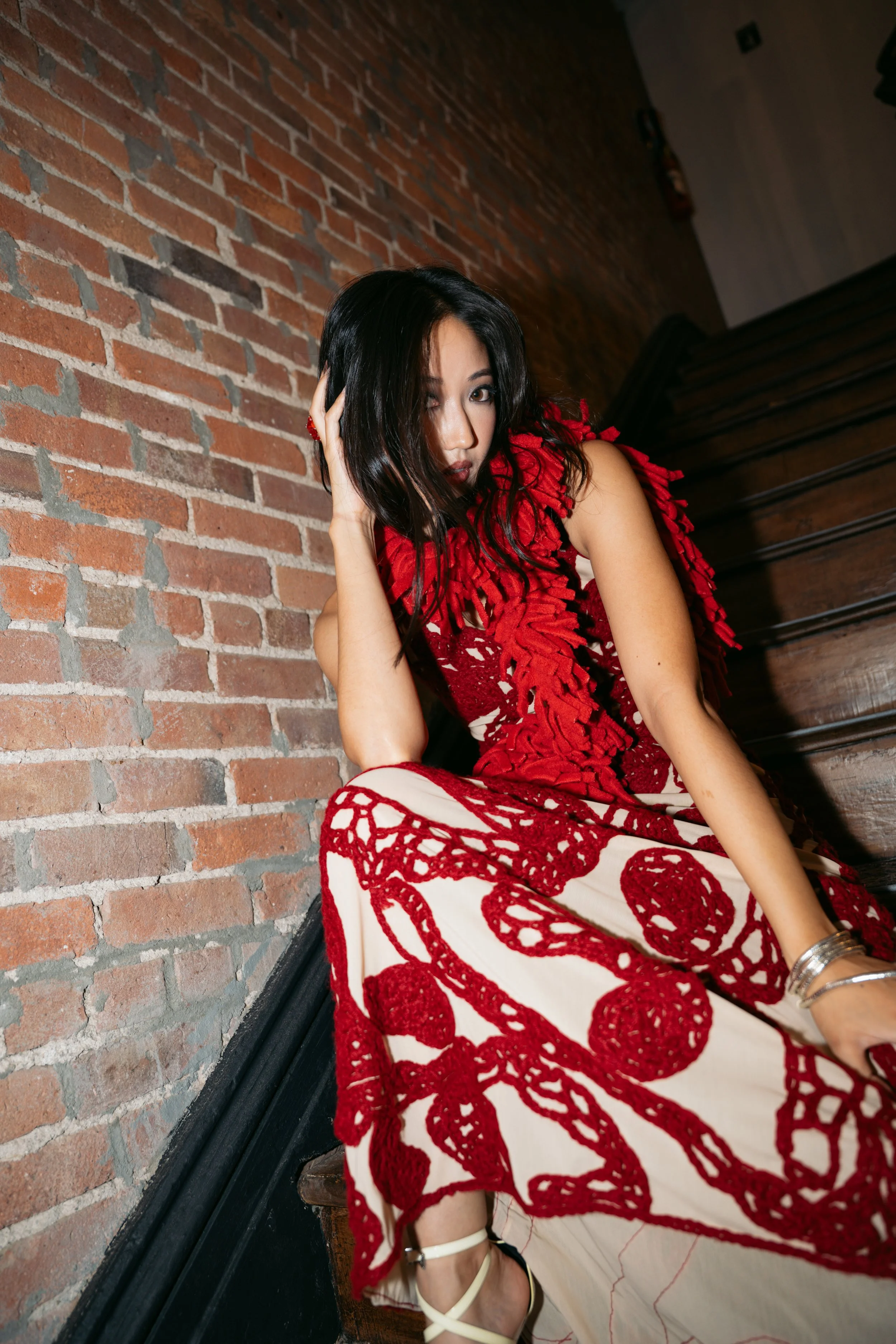 A woman in a red and white dress sitting next to a brick wall and staircase.