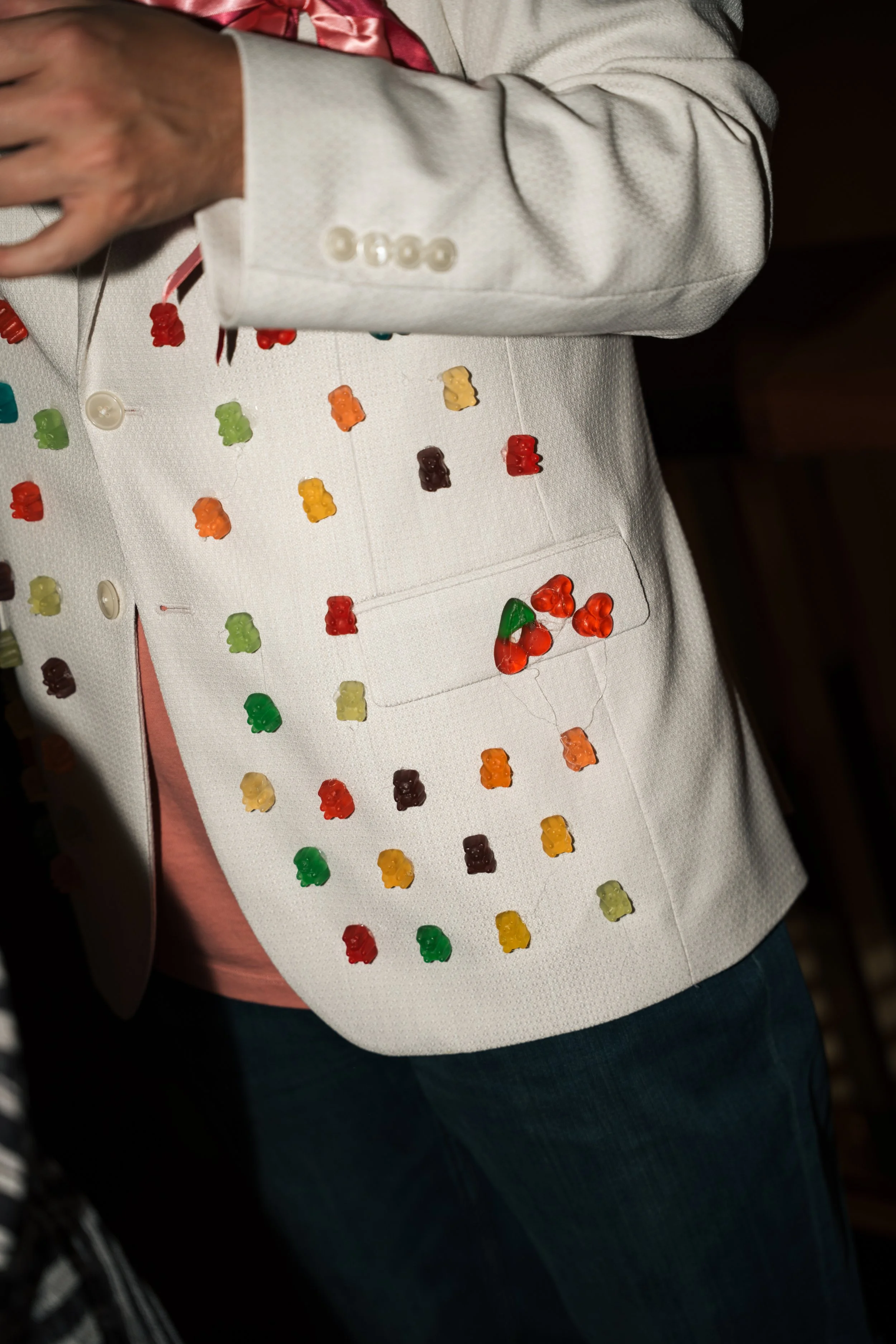 Person wearing a white vest decorated with colorful gummy bears and jelly beans, with a gray suit jacket on top.
