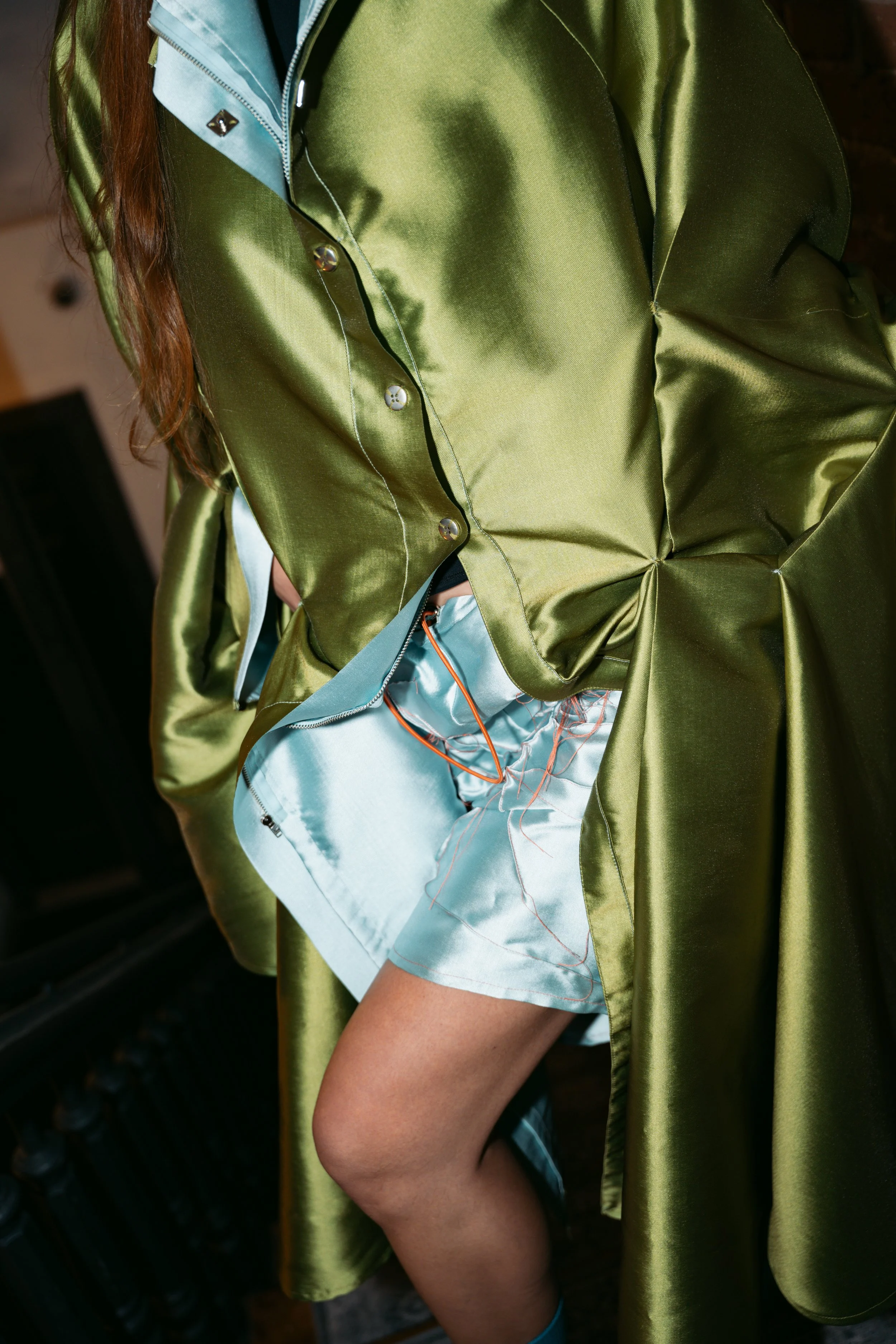 Close-up of a person wearing a shiny green satin dress with a blue lining, revealing their leg and part of their thigh.
