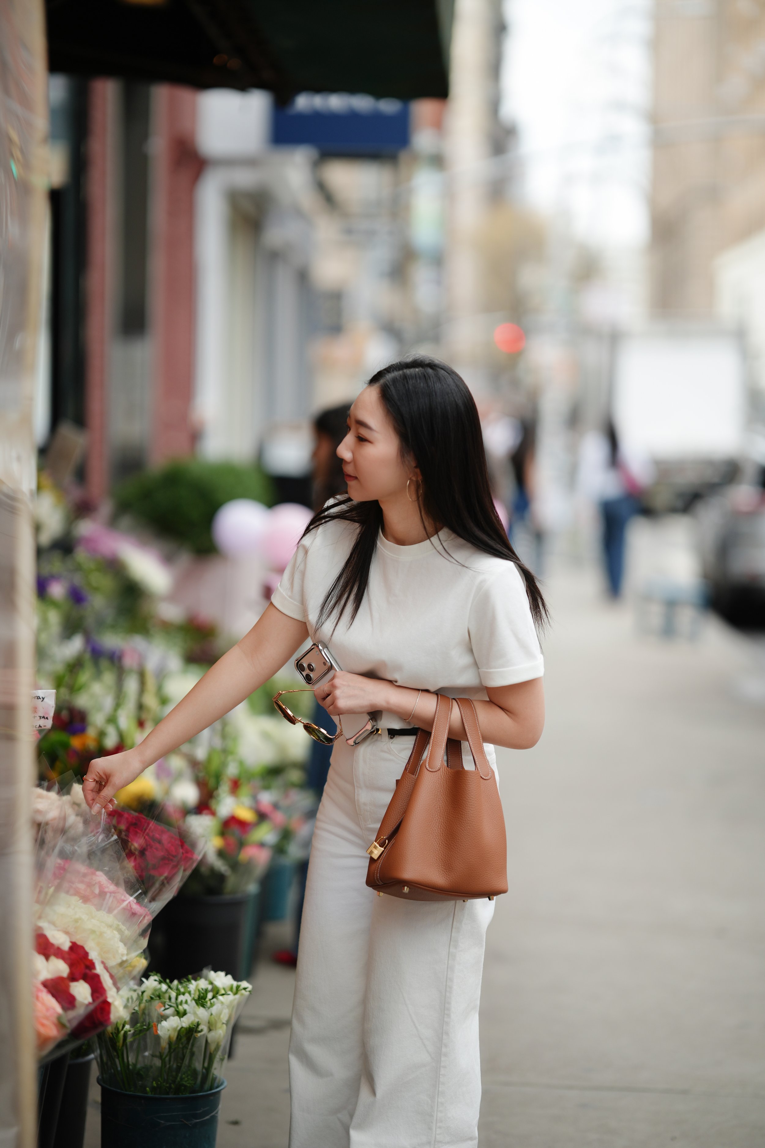 A woman in a white outfit shopping for flowers on a sidewalk.
