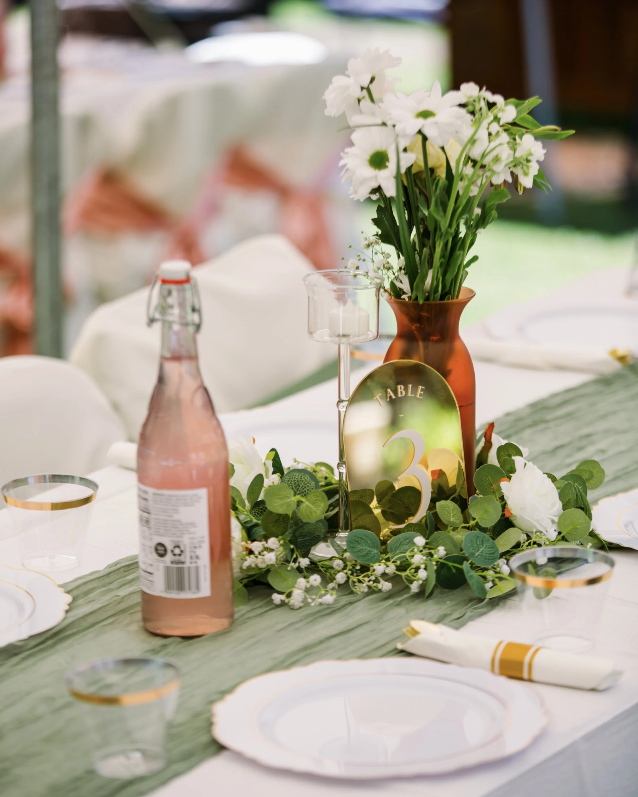 A centerpiece with white flowers and greenery on a table at a celebration or event, with plates and cups set for guests.