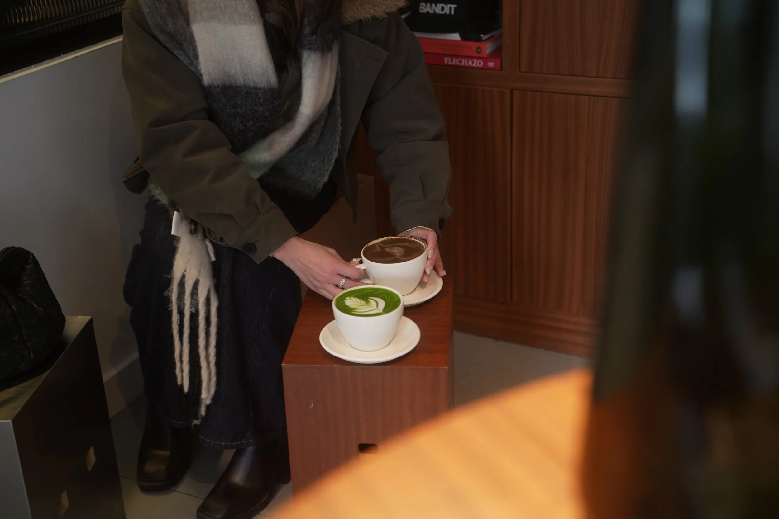 Person holding a cup of hot chocolate or coffee with latte art, standing next to two other cups with green and brown toppings on white saucers.