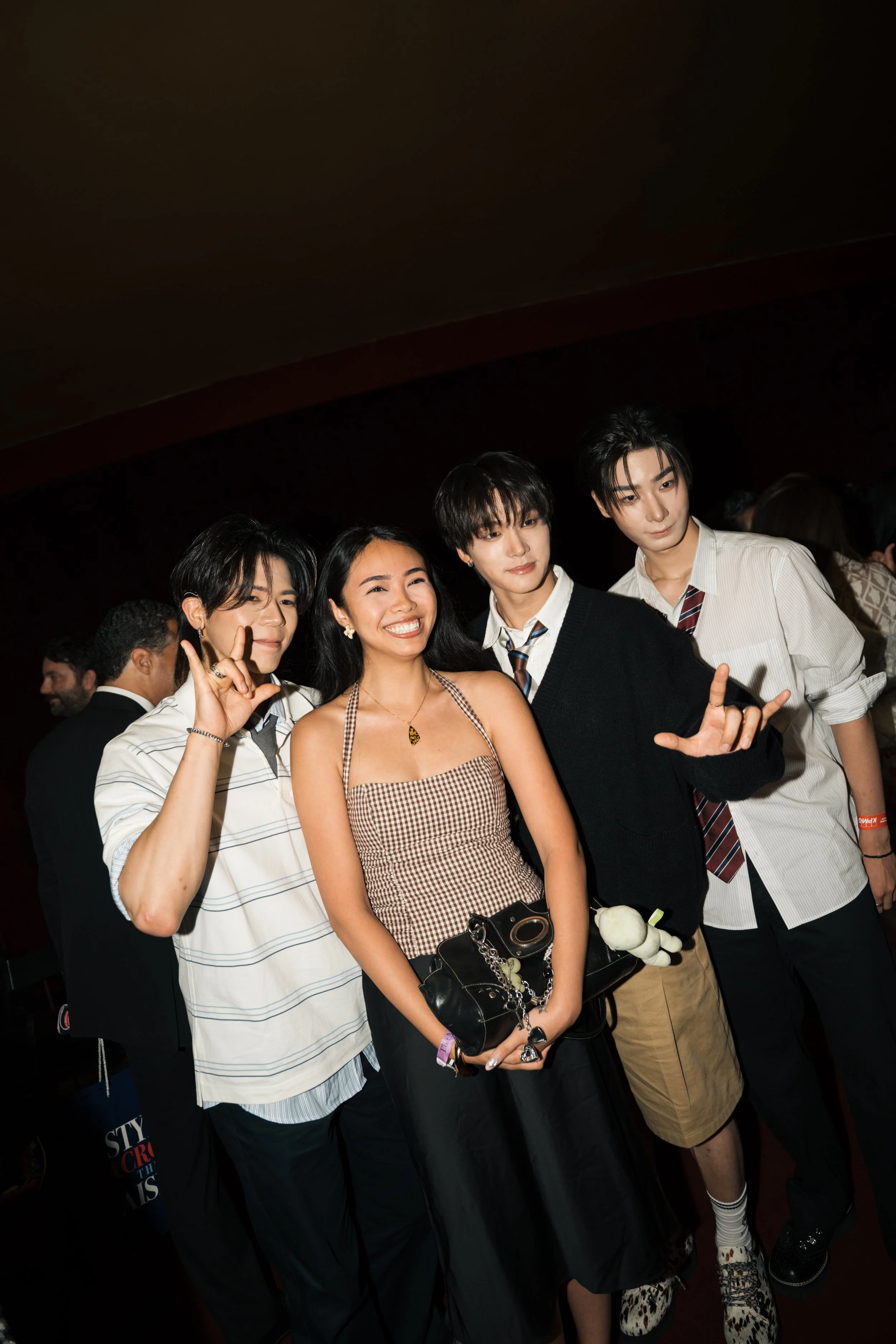 Group of four young people posing together at an indoor event, smiling and making hand gestures.