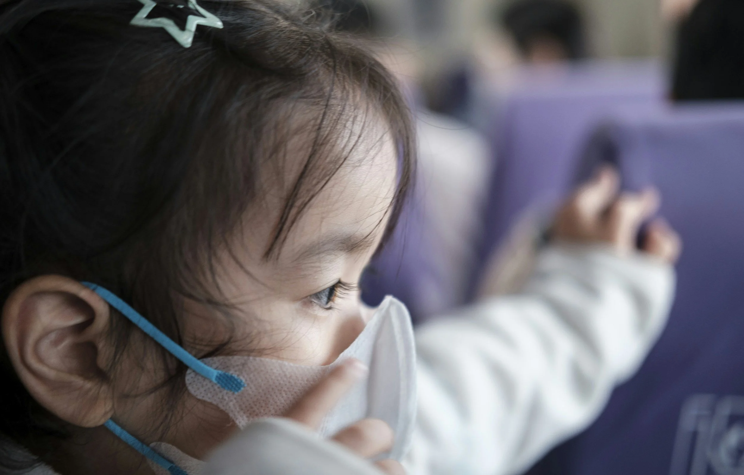 Close-up of a young girl with brown hair wearing a mask and a star-shaped hairpin, focused on an activity.