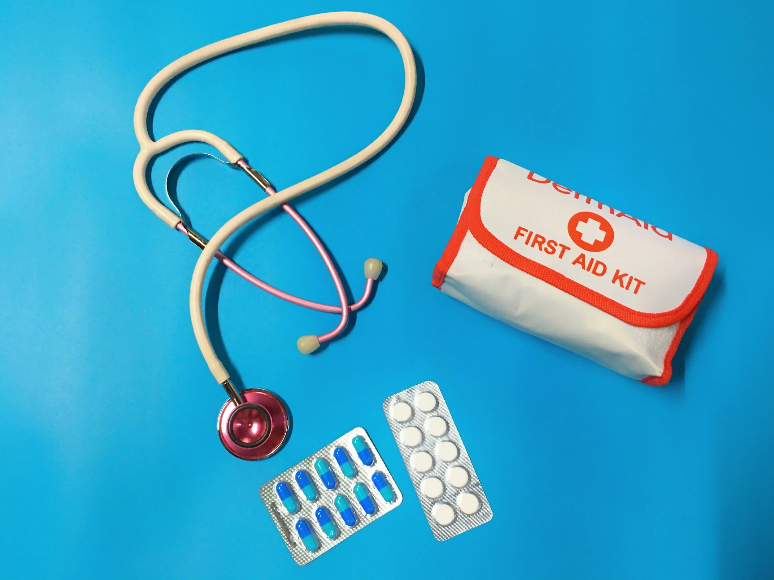 Medical stethoscope, blister packs of blue and white capsules, blister packs of white pills, a first aid kit, and medication bottles on a blue background.