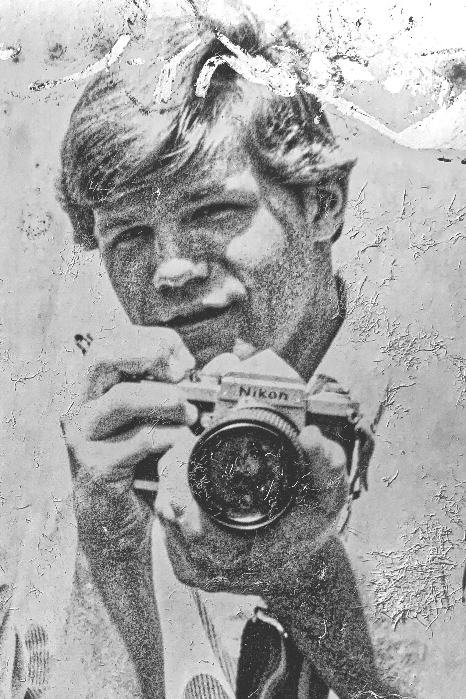 A black and white photo of a person with short hair taking a self-portrait with a Nikon camera, standing outdoors next to a dog.