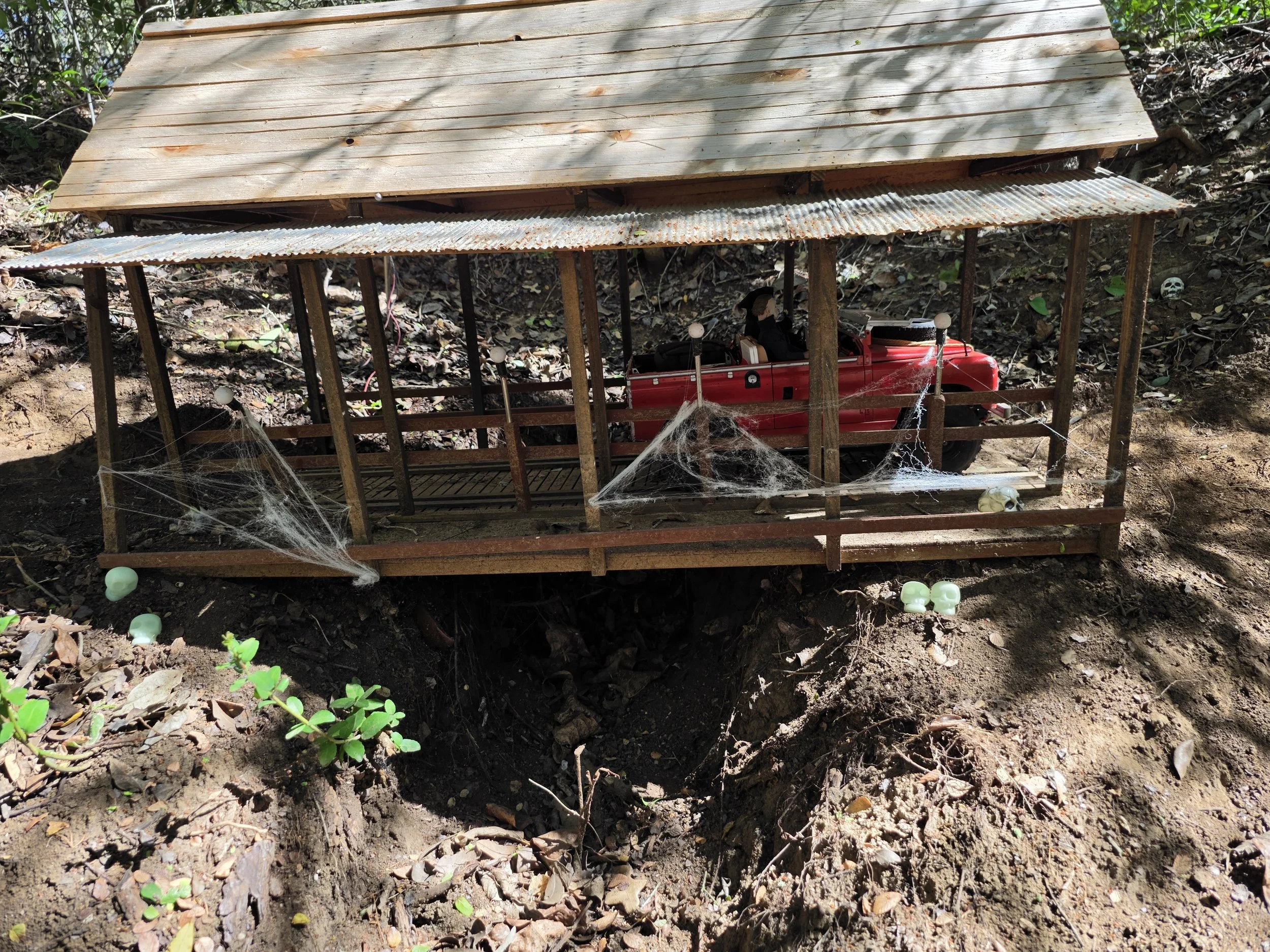 A red Boom RC Truck driving along a miniature covered wooden bridge containing cobwebs on the bridge railing.