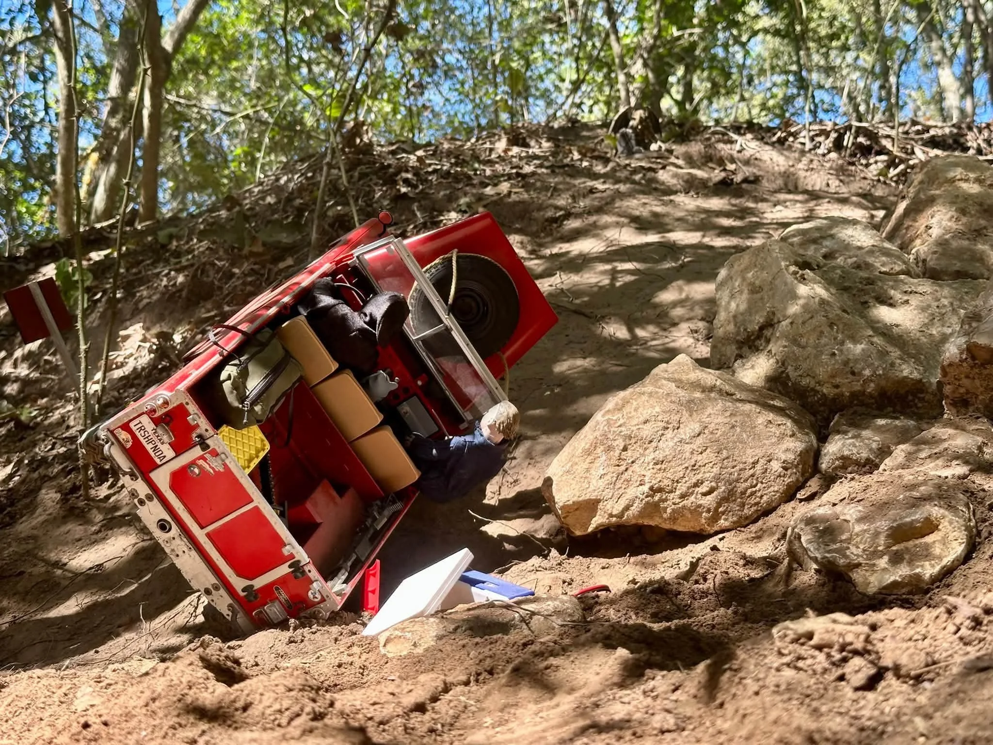 A rolled over RC Crawler Boom truck with scattered items, a scale cooler  toppled over and the hood ajar.