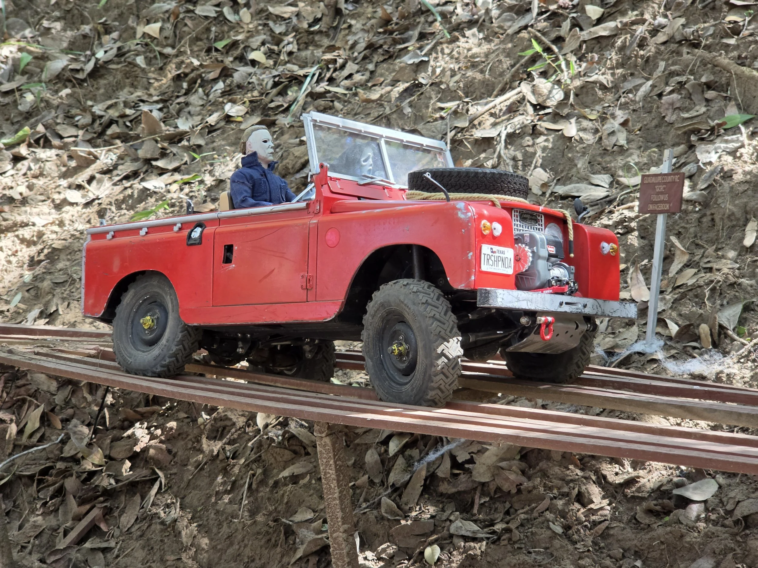 A red RC scale Boom truck driving along a miniature wooden bridge.with Michael Meyers in the passenger seat.  
