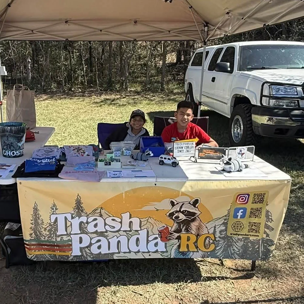 Trash Panda RC booth with two children sitting under the canopy at the table with the Trash Panda RC banner featuring the TPRC Raccoon.
