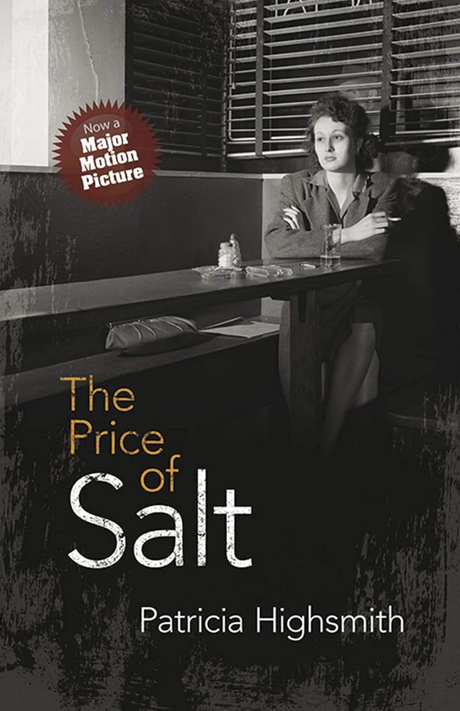 Black and white promotional image for the book "The Price of Salt" by Patricia Highsmith. The image features a vintage style photograph of a woman with curly hair sitting inside a diner, with a salt shaker and a glass of drink on the table. A red starburst logo on the left side states, "Now a Major Motion Picture."
