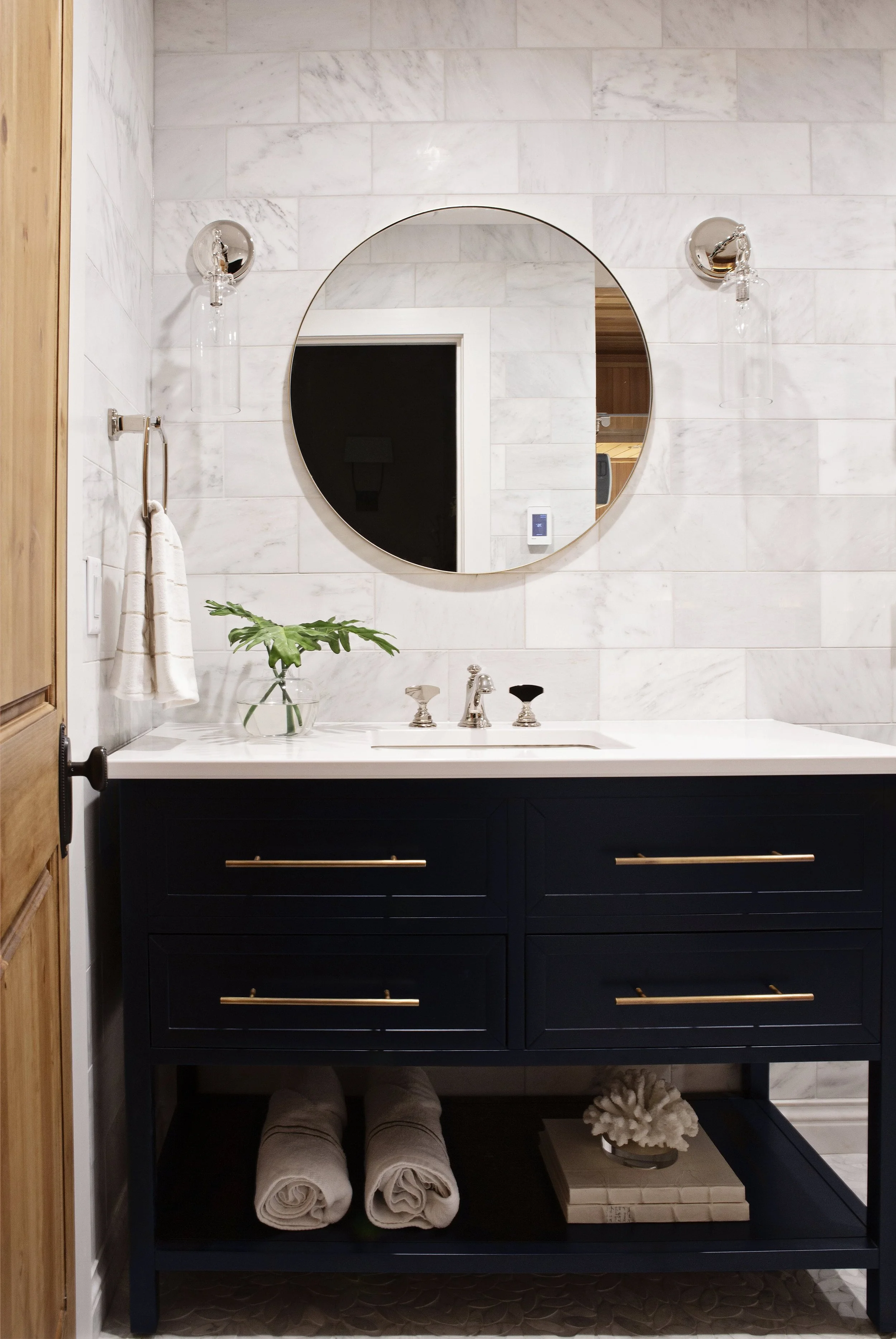 Navy vanity with round mirror at the bathroom entry, Overland Park, Kansas.