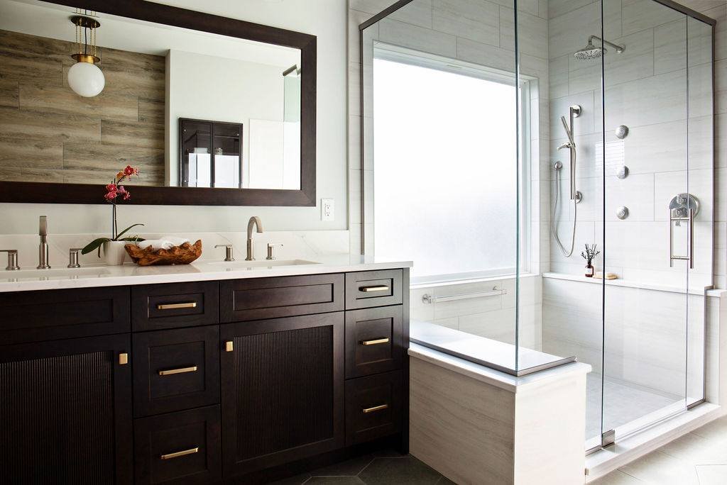 Dark wood double vanity with travertine-look tile and glass shower in Pleasant Hill MO primary bathroom renovation