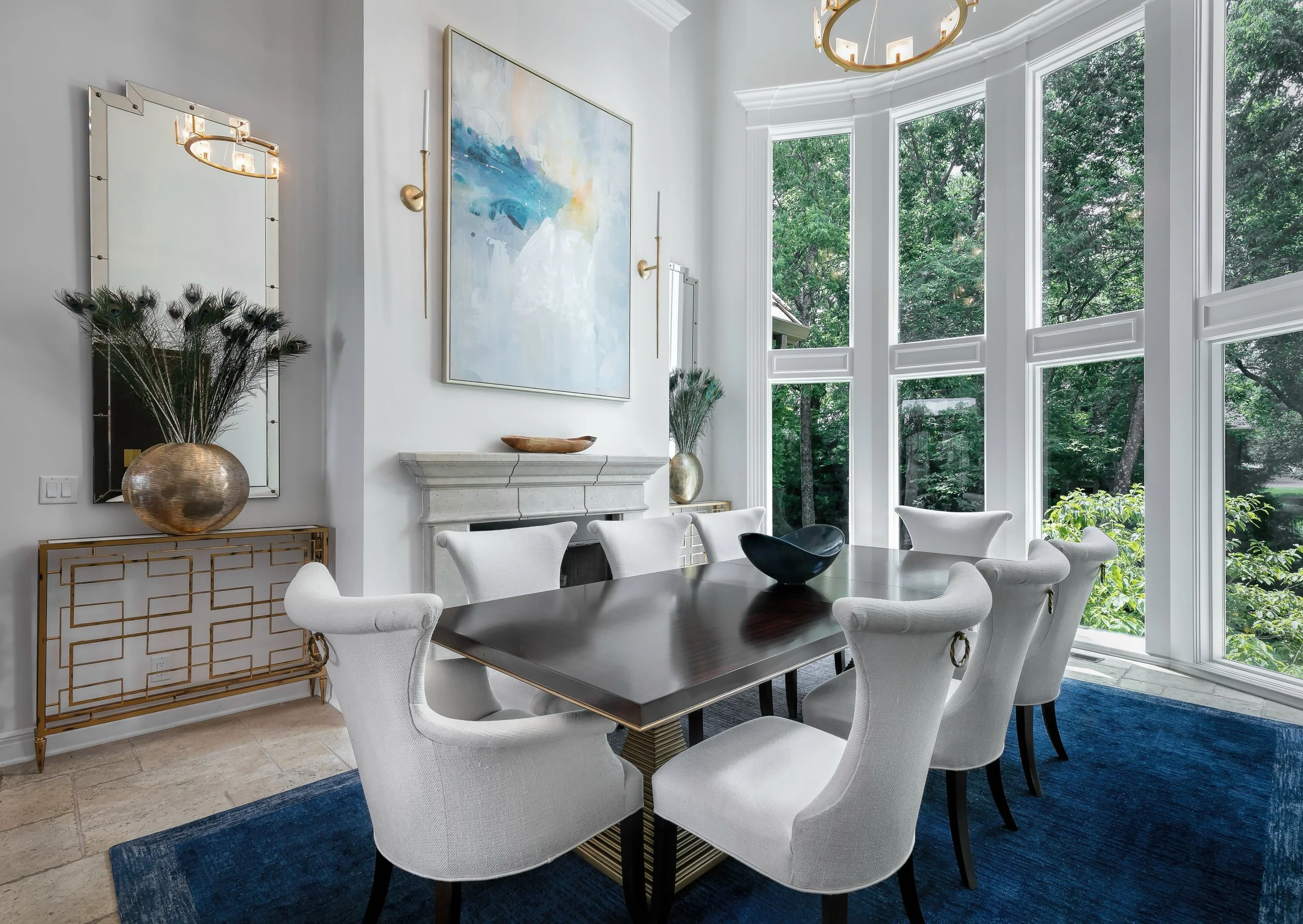 Contemporary dining room with white upholstered chairs, dark wood table, and blue abstract artwork above a stone fireplace