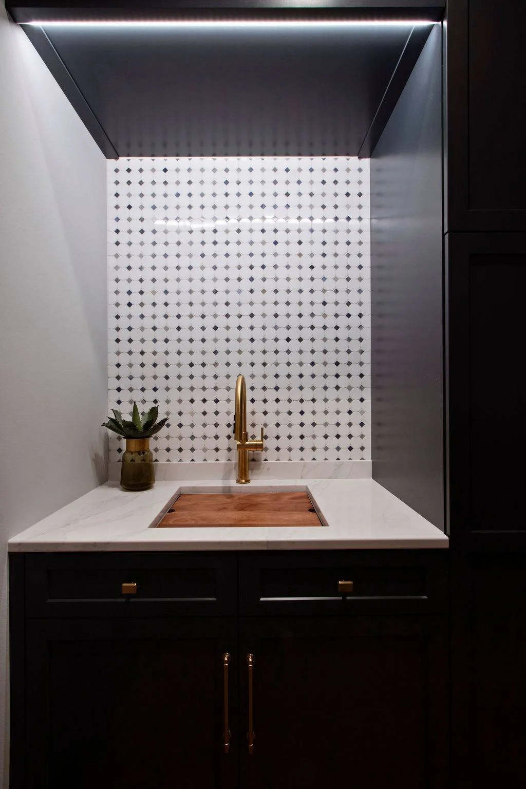 Laundry prep area with black cabinetry, brass faucet, marble countertop, and patterned tile backsplash