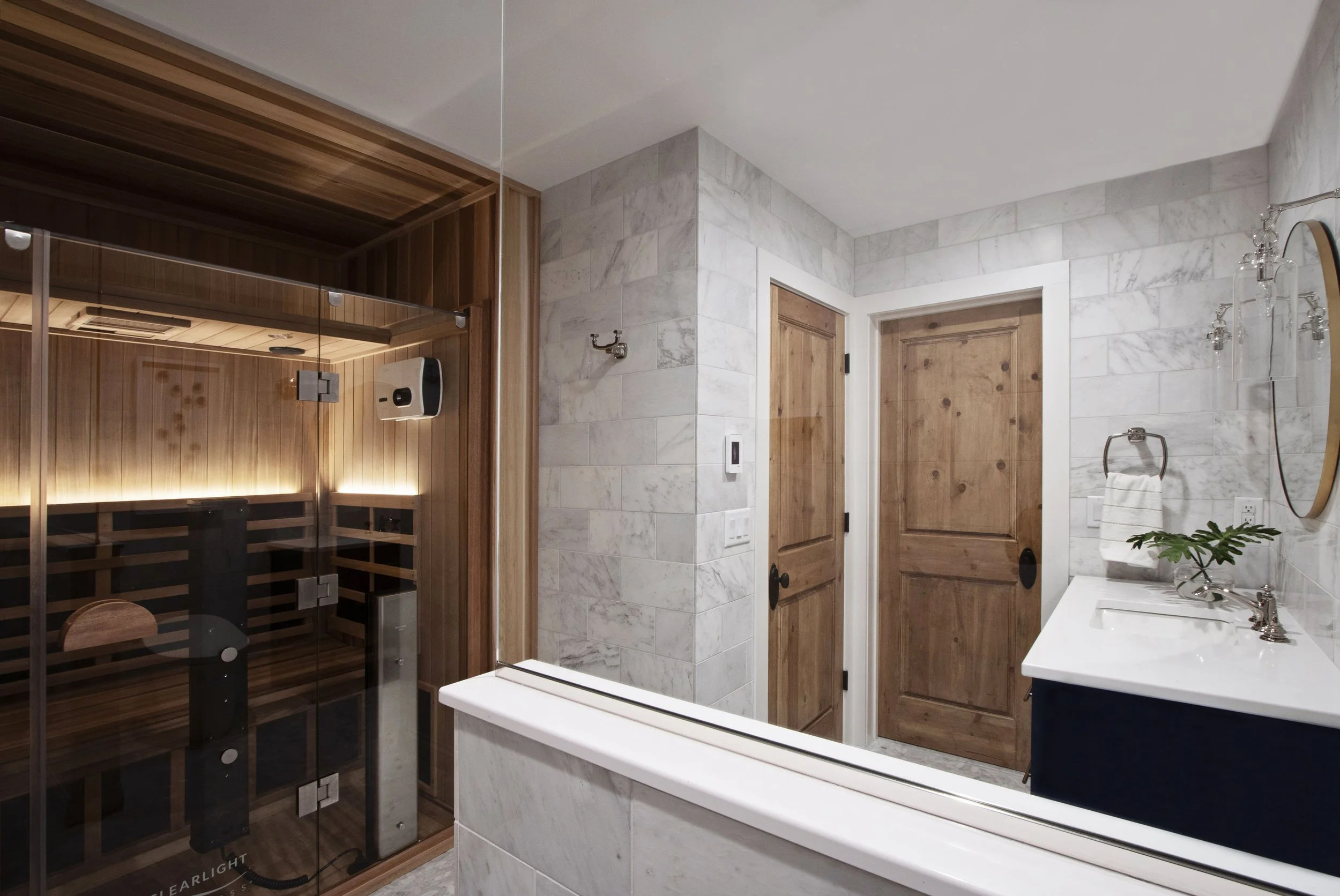 Luxury bathroom renovation with marble walls, warm wood detailing, custom vanity, and integrated home sauna