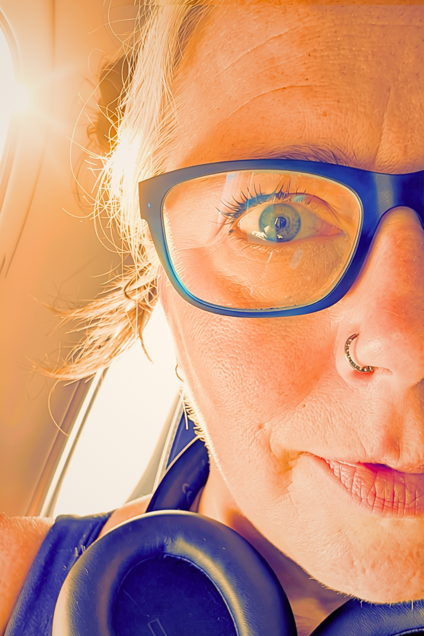 Close-up of a woman with glasses looking at a laptop, with blonde hair and a nose ring, illuminated by bright light.