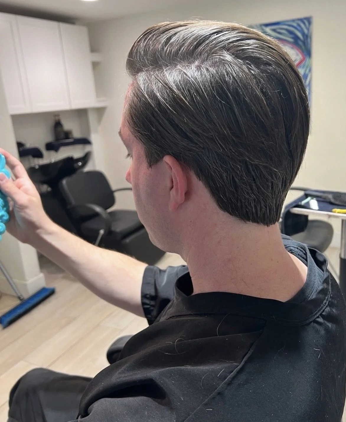 A white man with short dark hair, sitting in a salon chair getting a scissor haircut for men