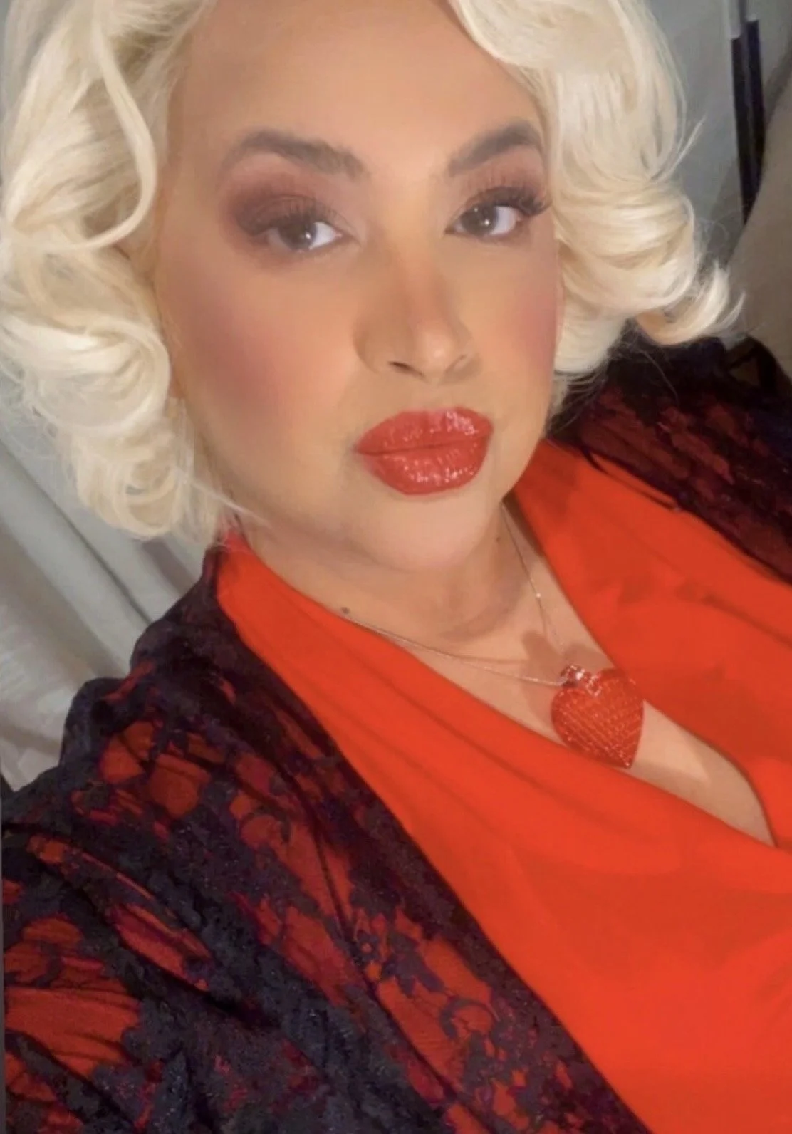 A white woman with platinum blonde curly hair, red lipstick, and makeup, wearing a blowout style with thermal curls