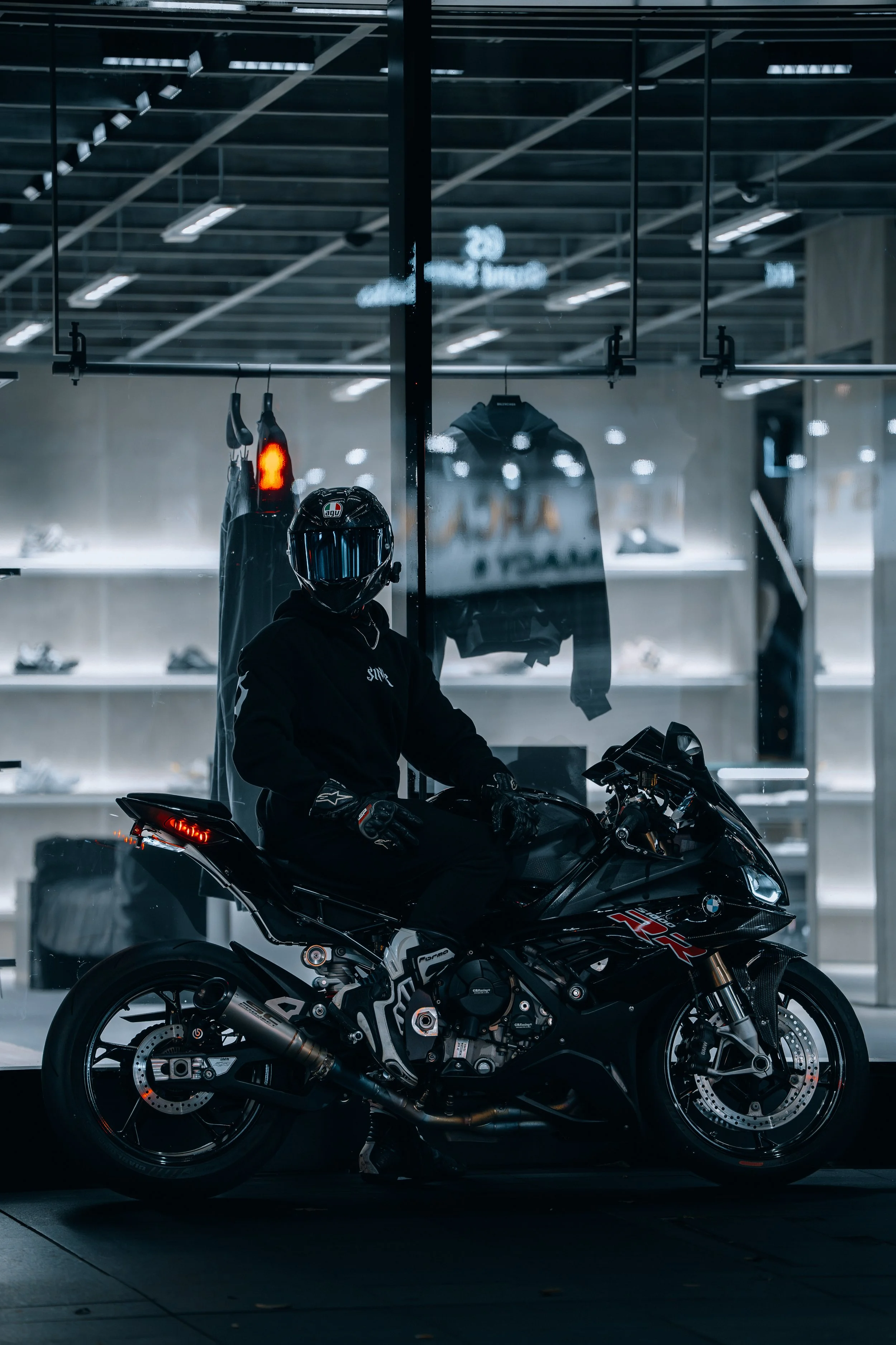 Person wearing a helmet sitting on a black BMW motorcycle inside a showroom, with windows and shelves behind.