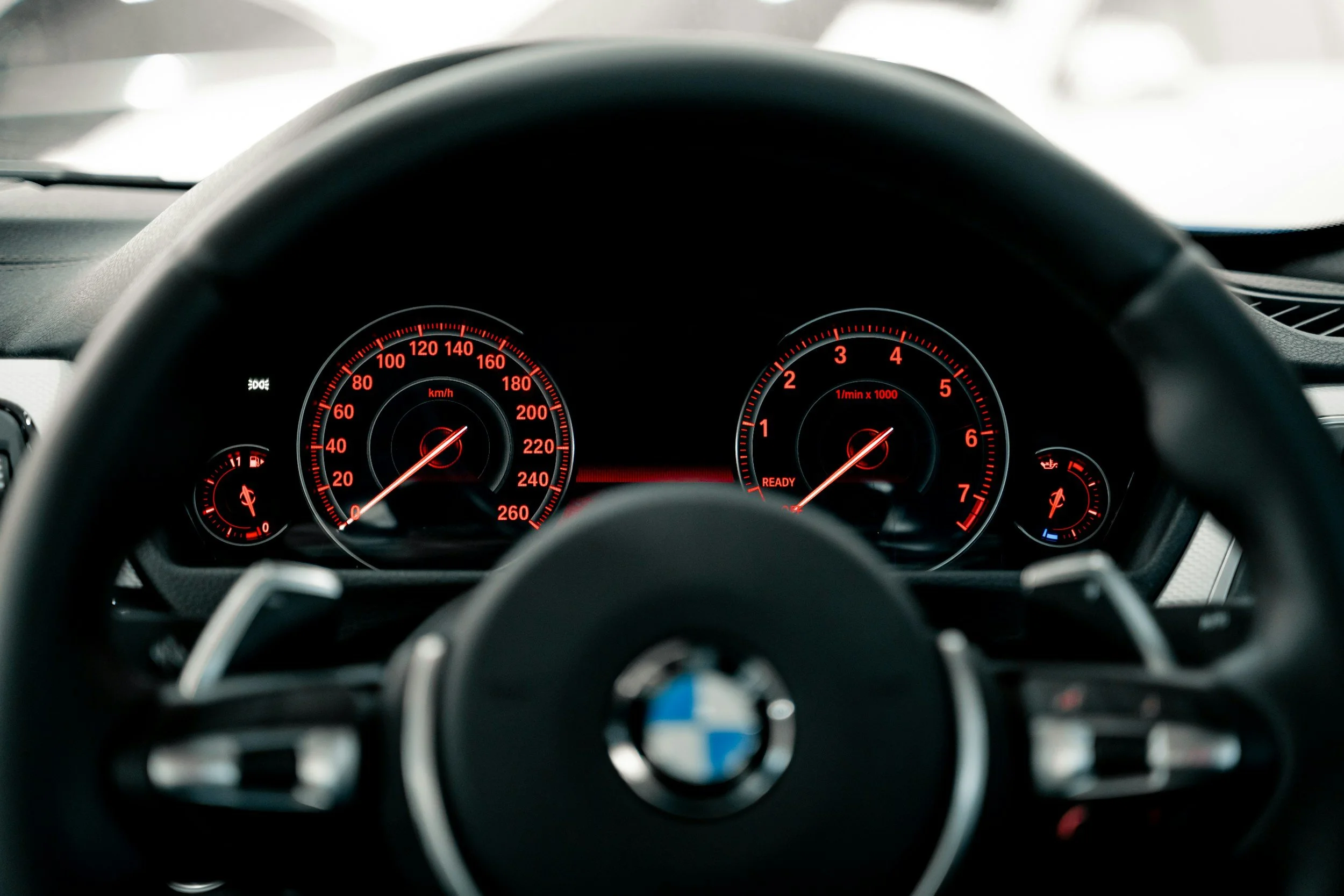 View from the driver's seat of a BMW car, showing illuminated dashboard with speedometer, tachometer, and fuel gauge.