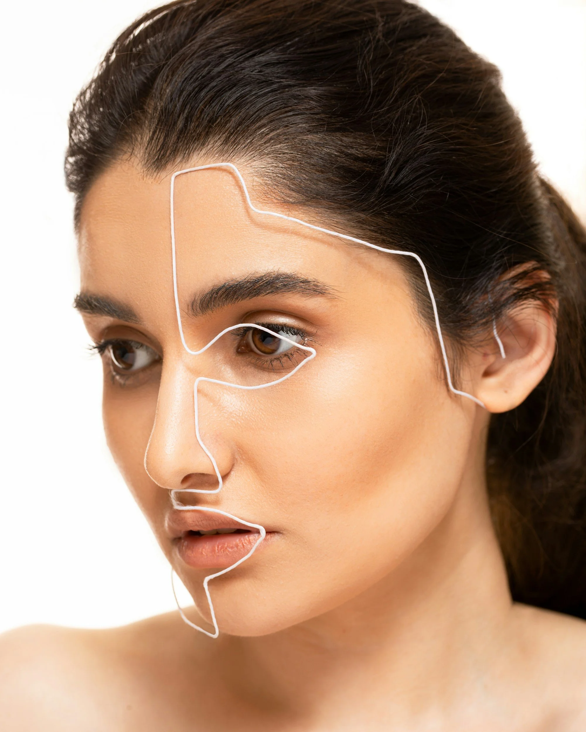 Close-up of a woman's face with white lines on her forehead, cheek, nose, and chin, indicating facial acupuncture points.
