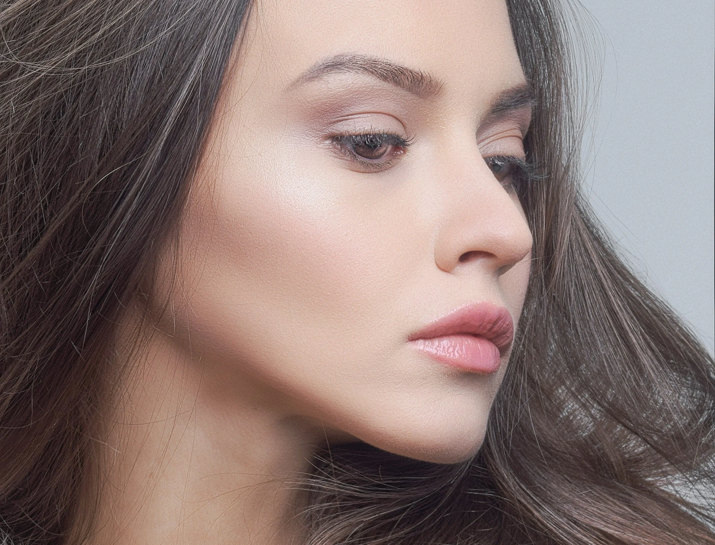 Close-up of a woman's face focusing on her eye, eyebrow, and lips with smooth skin and long brown hair.