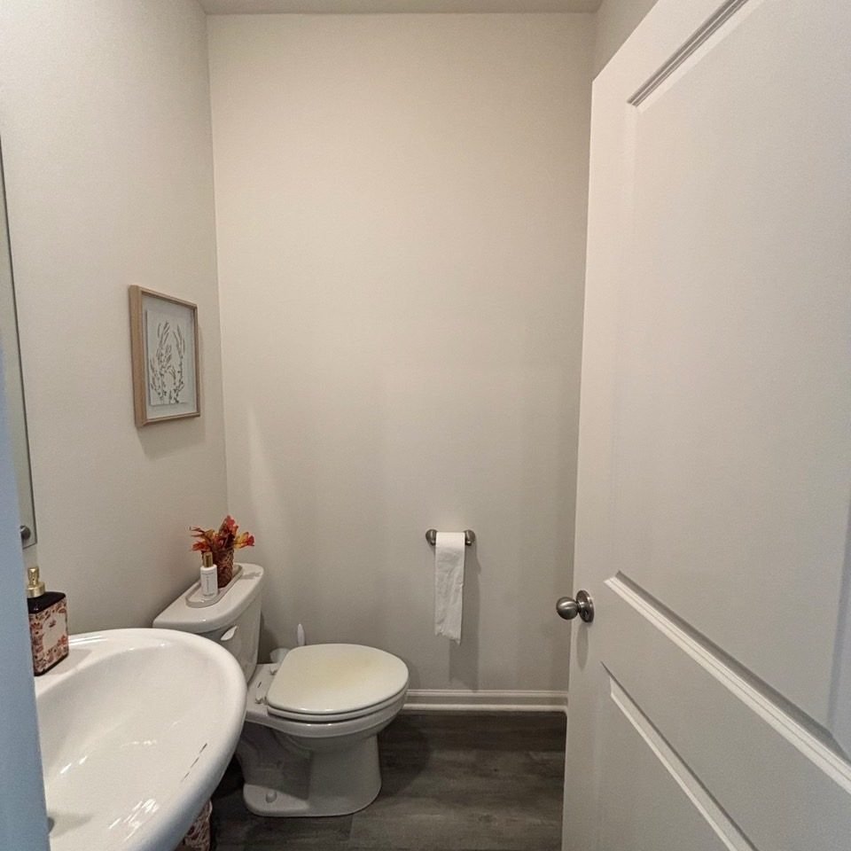 Before: powder room with painted walls, a pedestal sink, a toilet, and dark flooring.