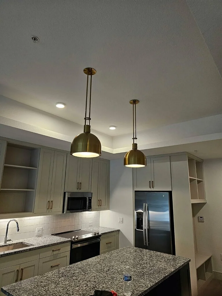 Modern kitchen with grey cabinets, granite countertops, stainless steel appliances, and two gold pendant lights hanging above an island.