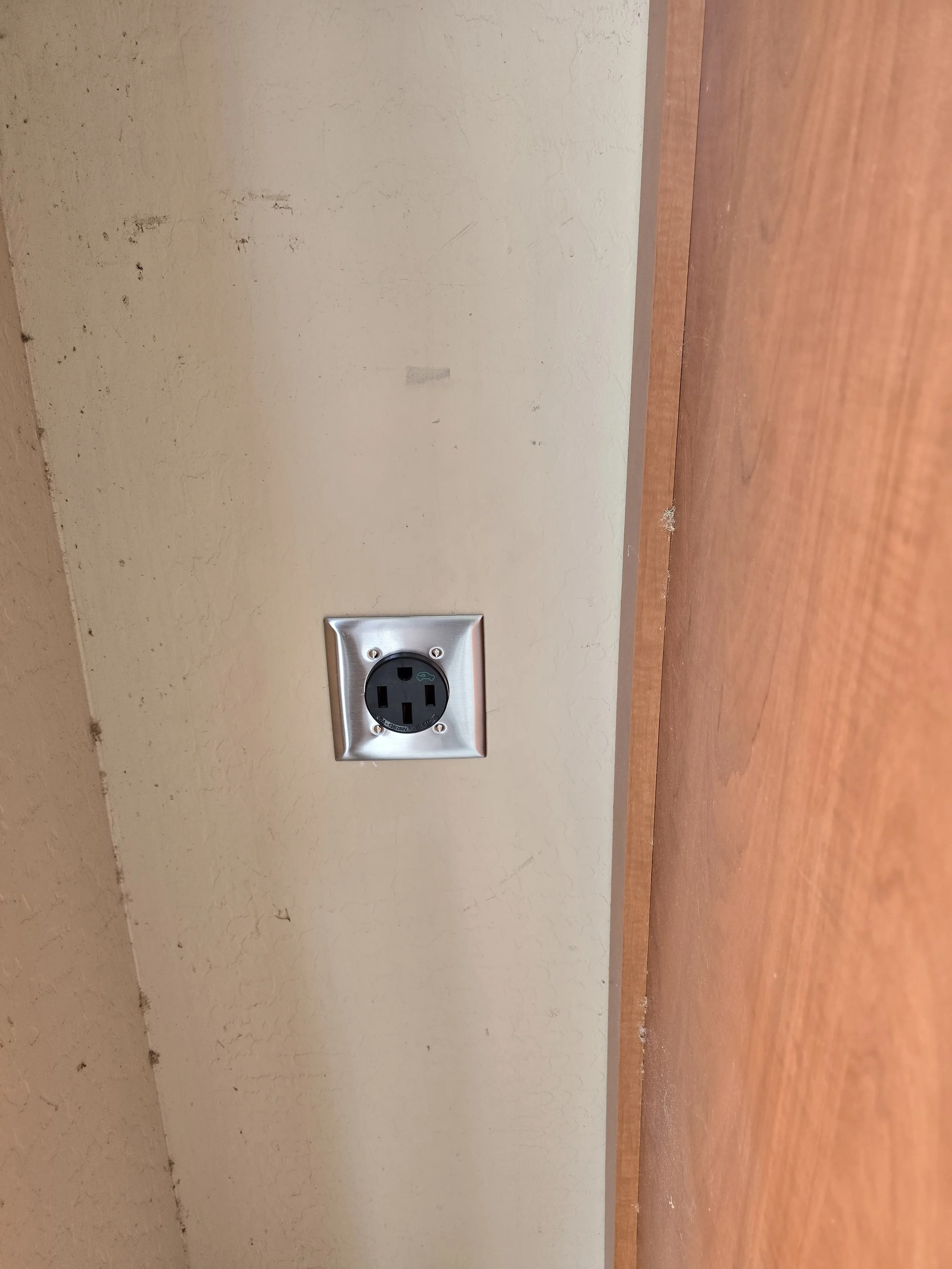 A standard electrical power outlet on a beige-colored wall, with a wooden surface in the foreground.