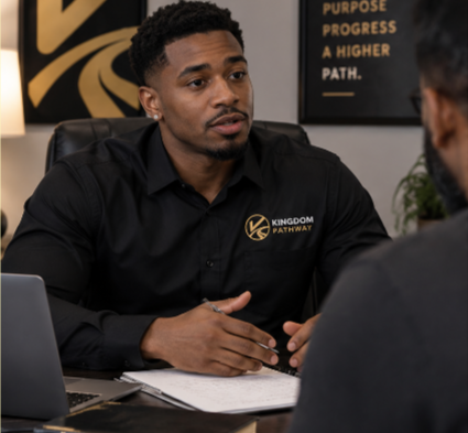 Man wearing a black Kingdom Pathway branded shirt sitting at a desk during a consultation or meeting.