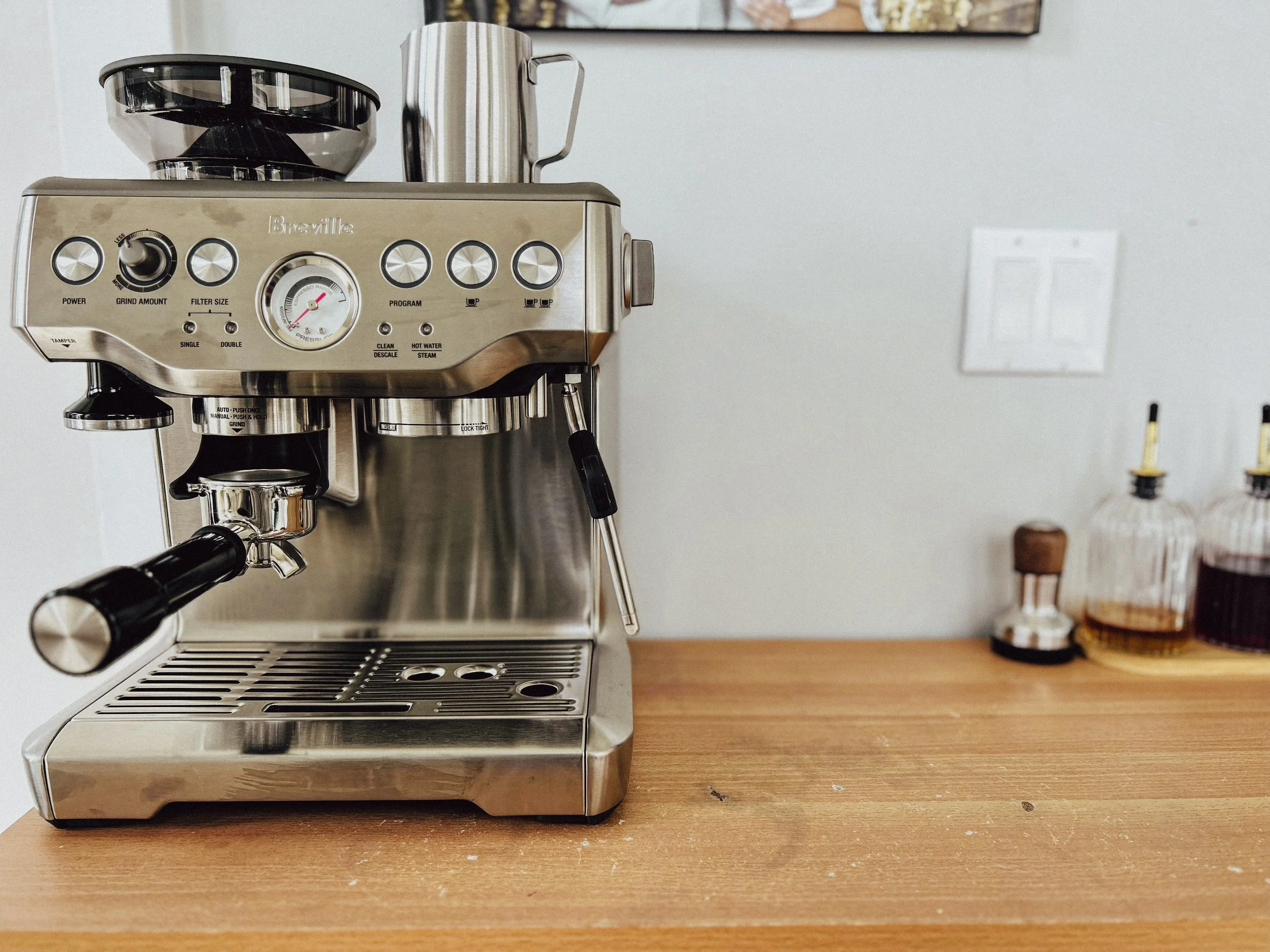 A silver espresso machine with black handles on a wooden countertop, with some small objects and a blurred background.